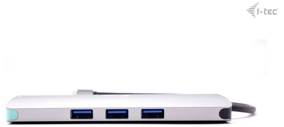 USB-C hub se třemi modrými USB porty. Vpravo nahoře je viditelné logo. Zařízení je stříbrné barvy a leží na bílém pozadí.