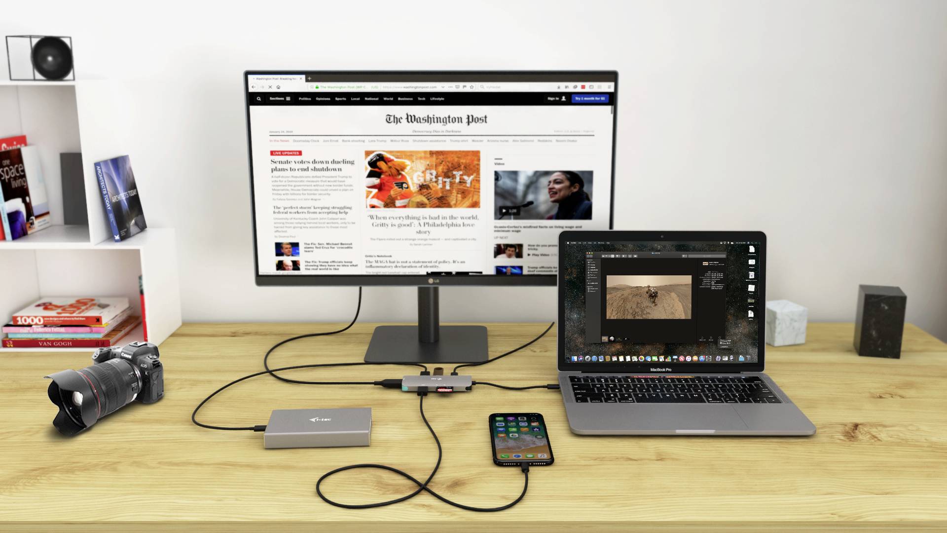 Psací stůl s monitorem zobrazujícím zpravodajský web, laptop s fotoeditačním programem, fotoaparát a smartphone.