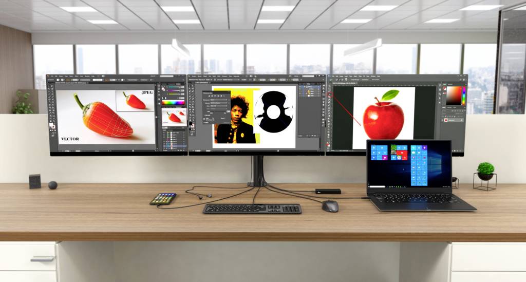 Pracoviště se třemi monitory a notebookem, zobrazující grafický designový software s obrázky ovoce a portrétů.