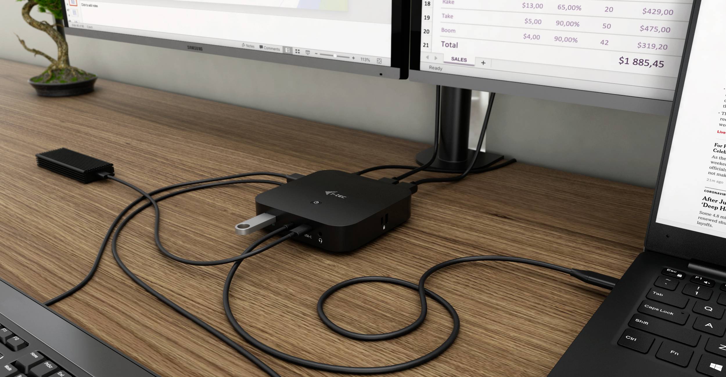 Počítačové pracoviště s notebookem, dvěma monitory a USB hubem na dřevěném psacím stole. Kabely propojují zařízení.