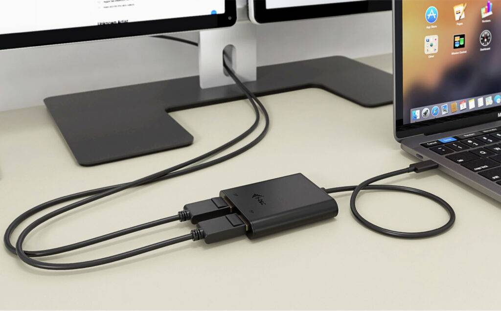 USB hub propojuje laptop se dvěma monitory na pracovním stole. Kabely jsou vedeny uspořádaně podél pracovní plochy.