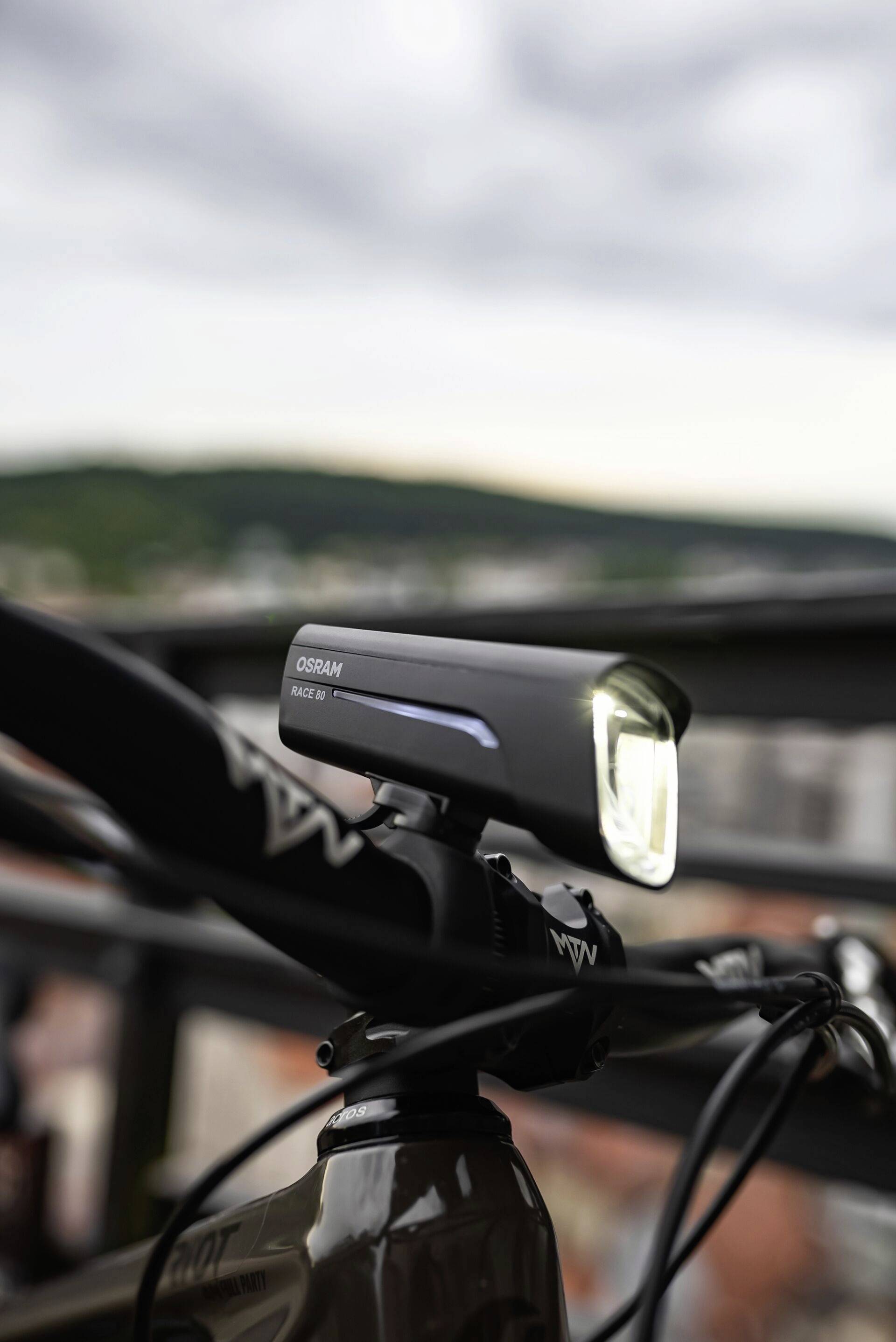 Jízdní kolo stojí na balkóně. V popředí je vidět zapnuté cyklistické světlo namontované na řídítkách.