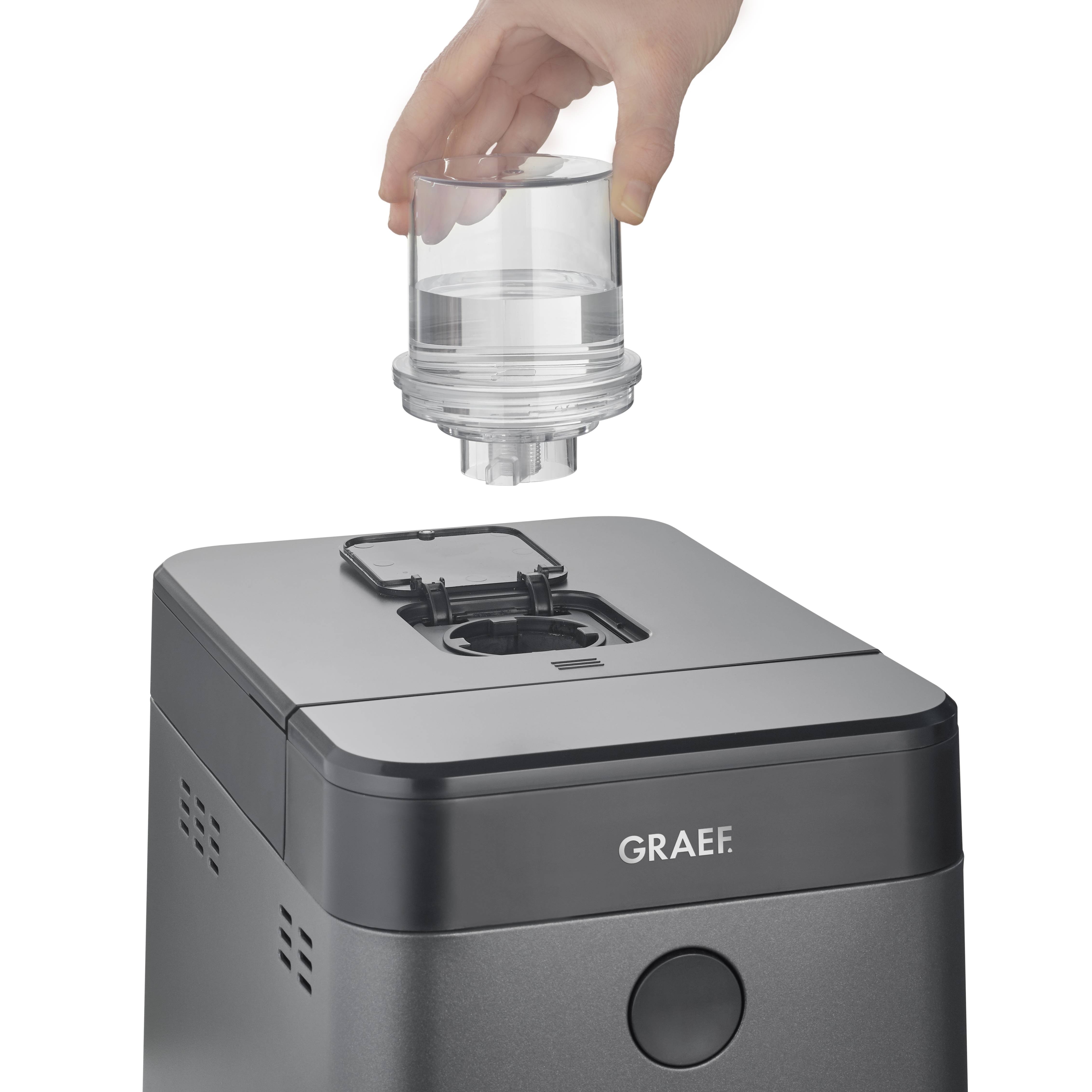Jedna ruka pokládá přílohu na šedý kuchyňský robot značky Graef.