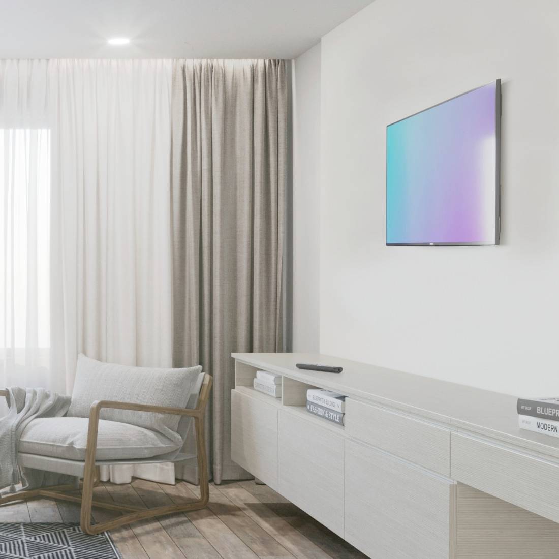 Obývací pokoj s moderní židlí, světlou záclonou, minimalistickou příborníkem, na němž jsou knihy, a na stěně plochý displej.