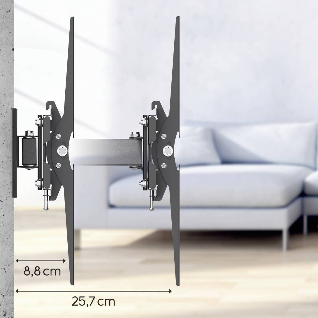 Nástěnný držák TV s rotačními rameny, připevněný na stěně. Vzdálenost od stěny: 8,8 cm. Maximální vysunutí: 25,7 cm. V pozadí sedací souprava.