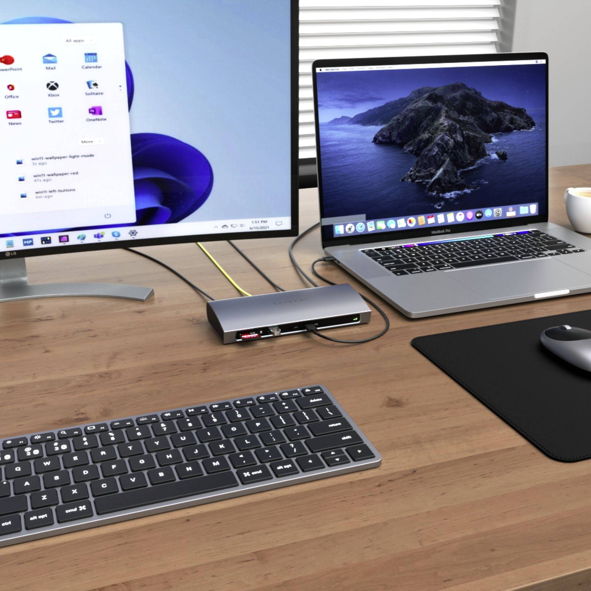 Psací stůl s monitorem zobrazujícím Windows, laptopem s macOS, dokovací stanicí, klávesnicí a myší.
