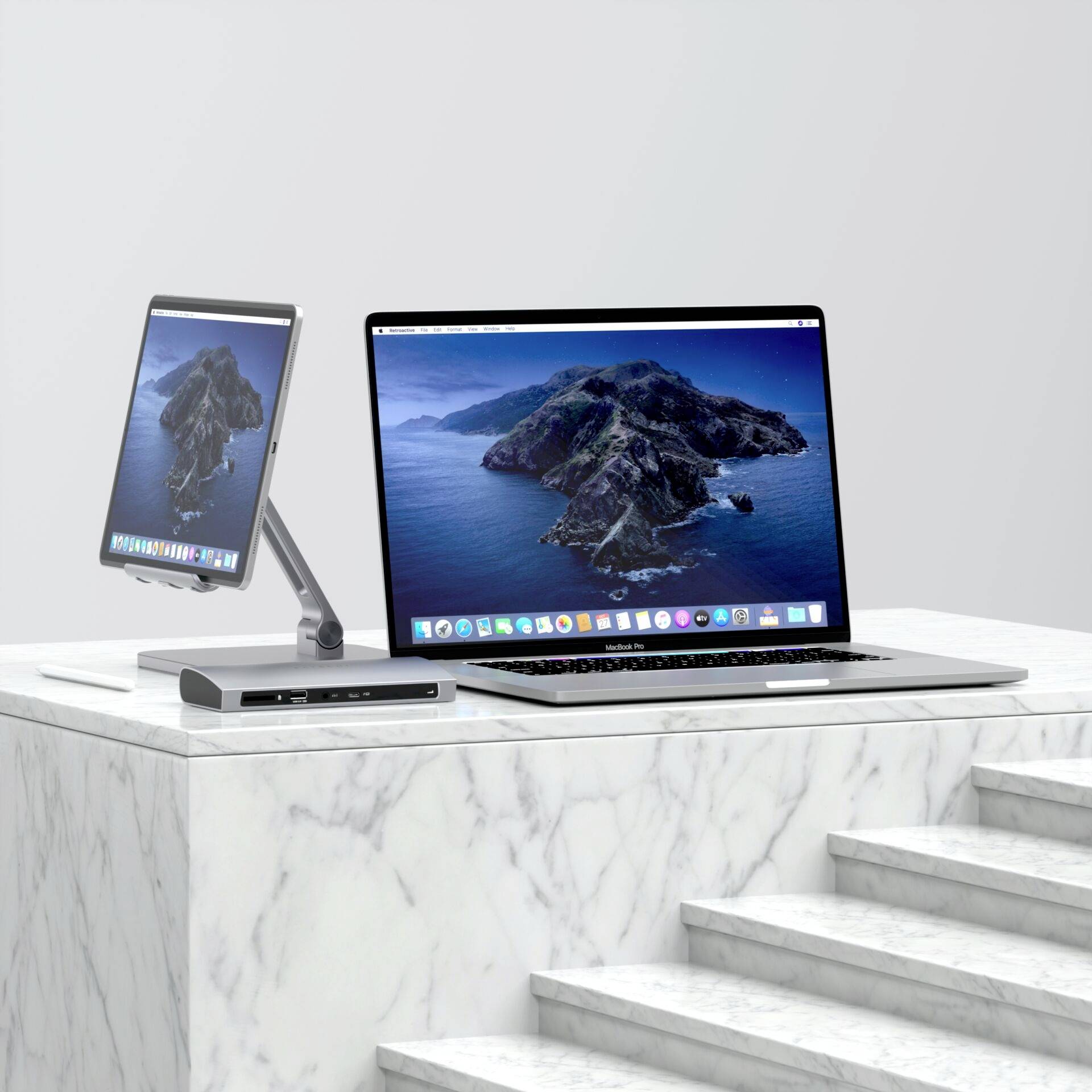 Laptop a tablet leží vedle sebe na mramorovém stole. Oba zobrazují krajinu s horami a mořem na obrazovce.