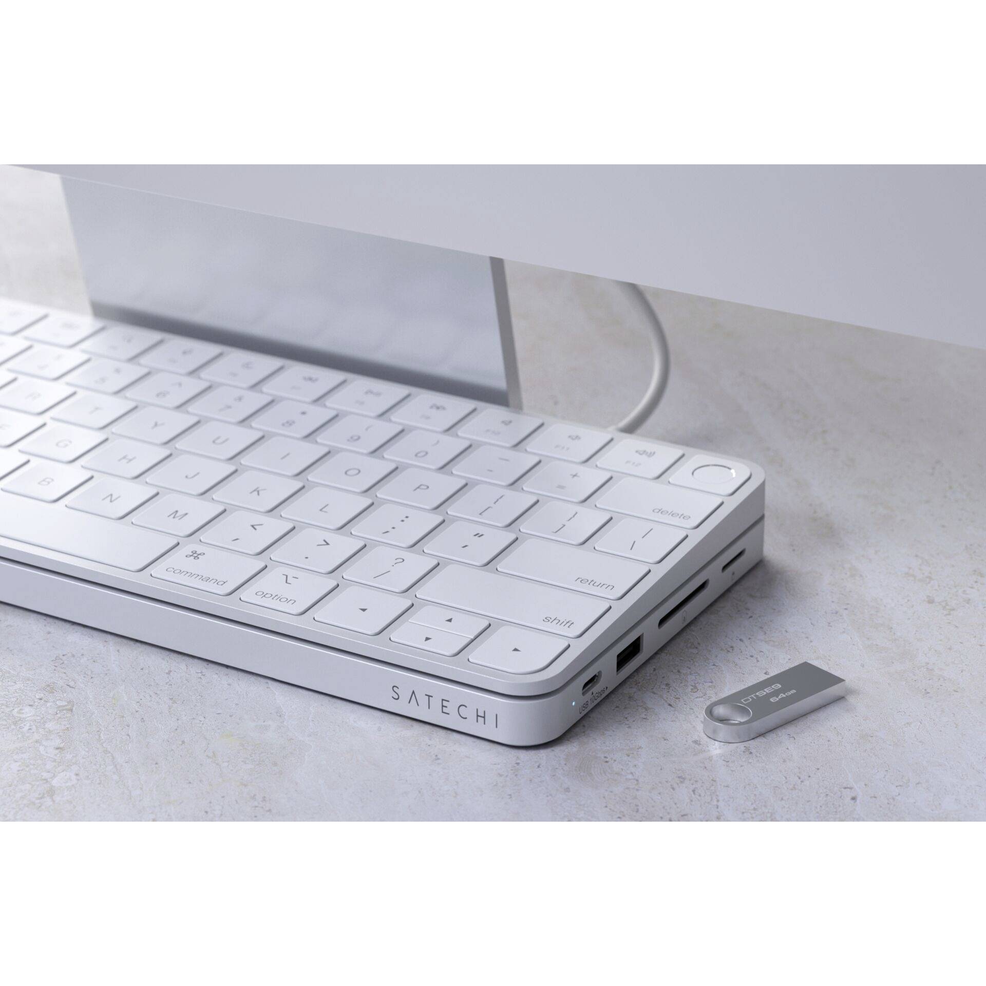 Bílá, plochá klávesnice s bočními konektory leží na stole. Vedle ní je malý USB přijímač.