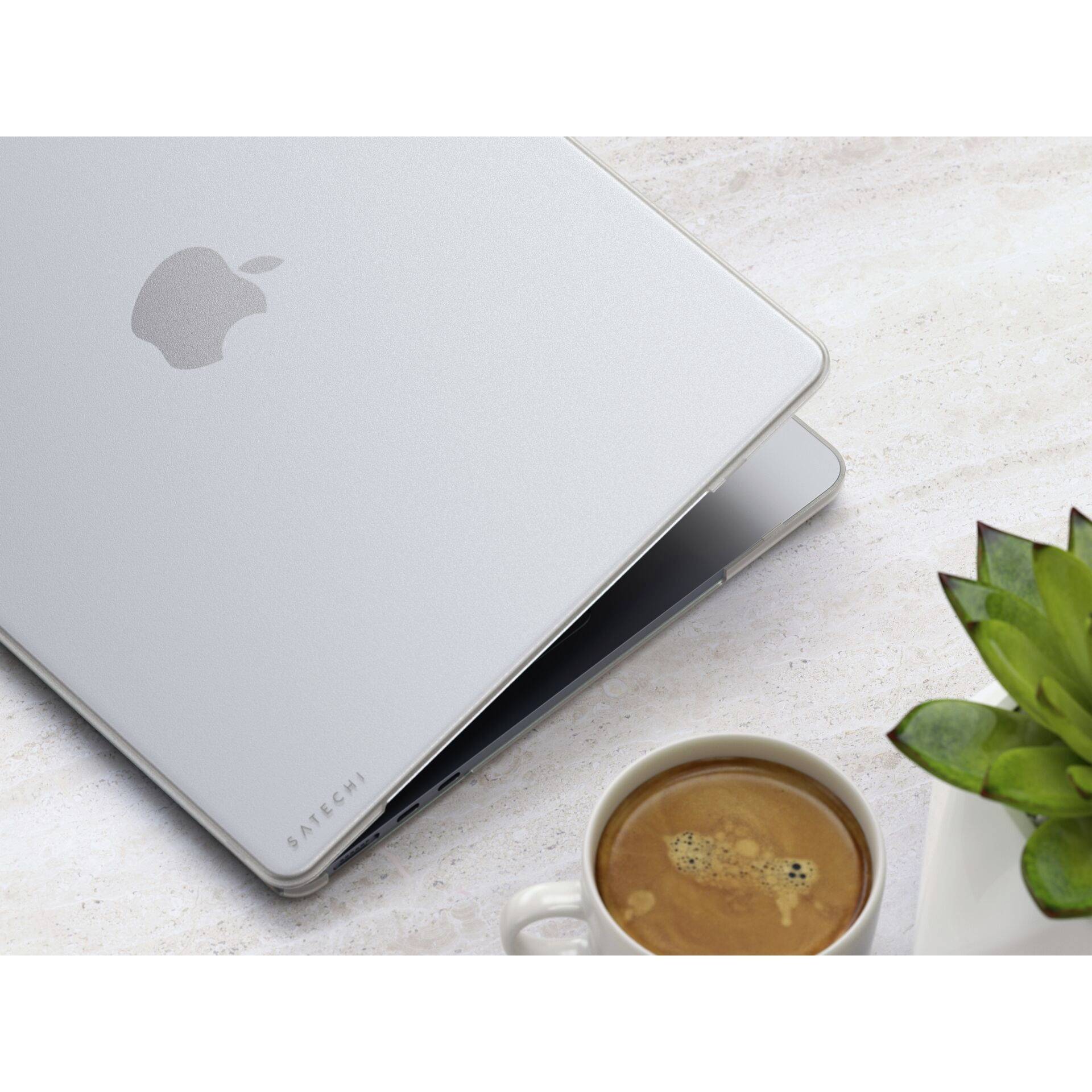 Laptop v stříbrném obalu částečně otevřený, vedle šálek kávy a rostlina na světlém stole.