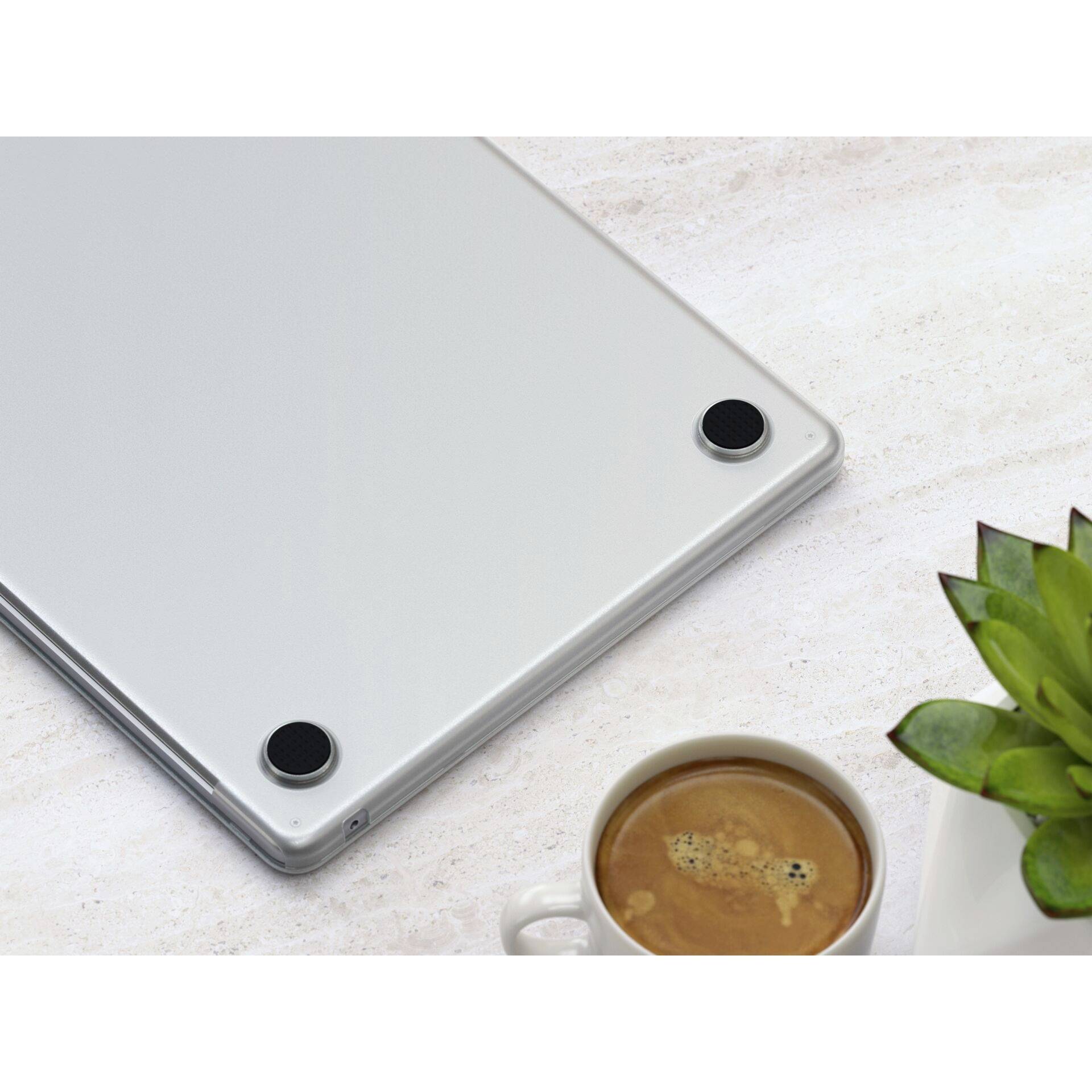 Šedý laptop se zaoblenými gumovými nožkami na stole, vedle zelená rostlina a šálek kávy. Tichý pracovní prostor.