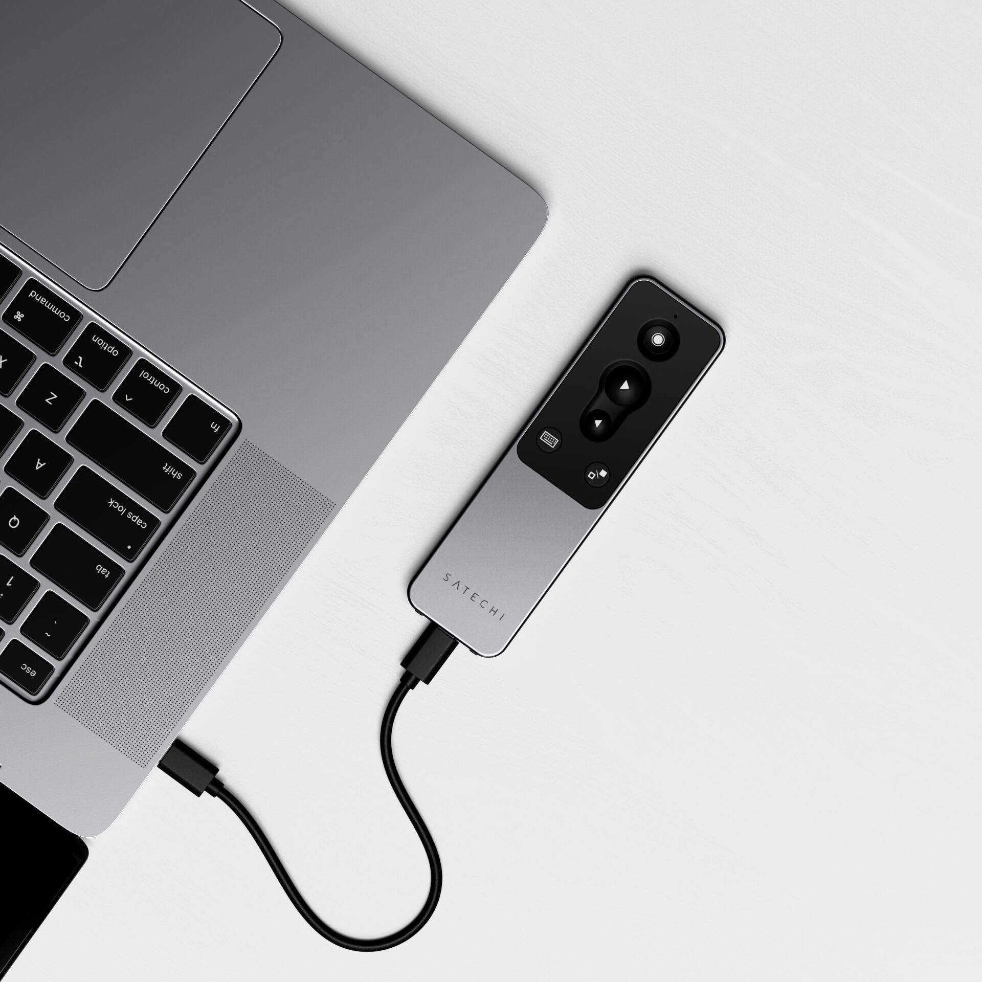 Laptop připojený k bezdrátovému prezentéru pomocí USB kabelu, ležící na bílém stole.