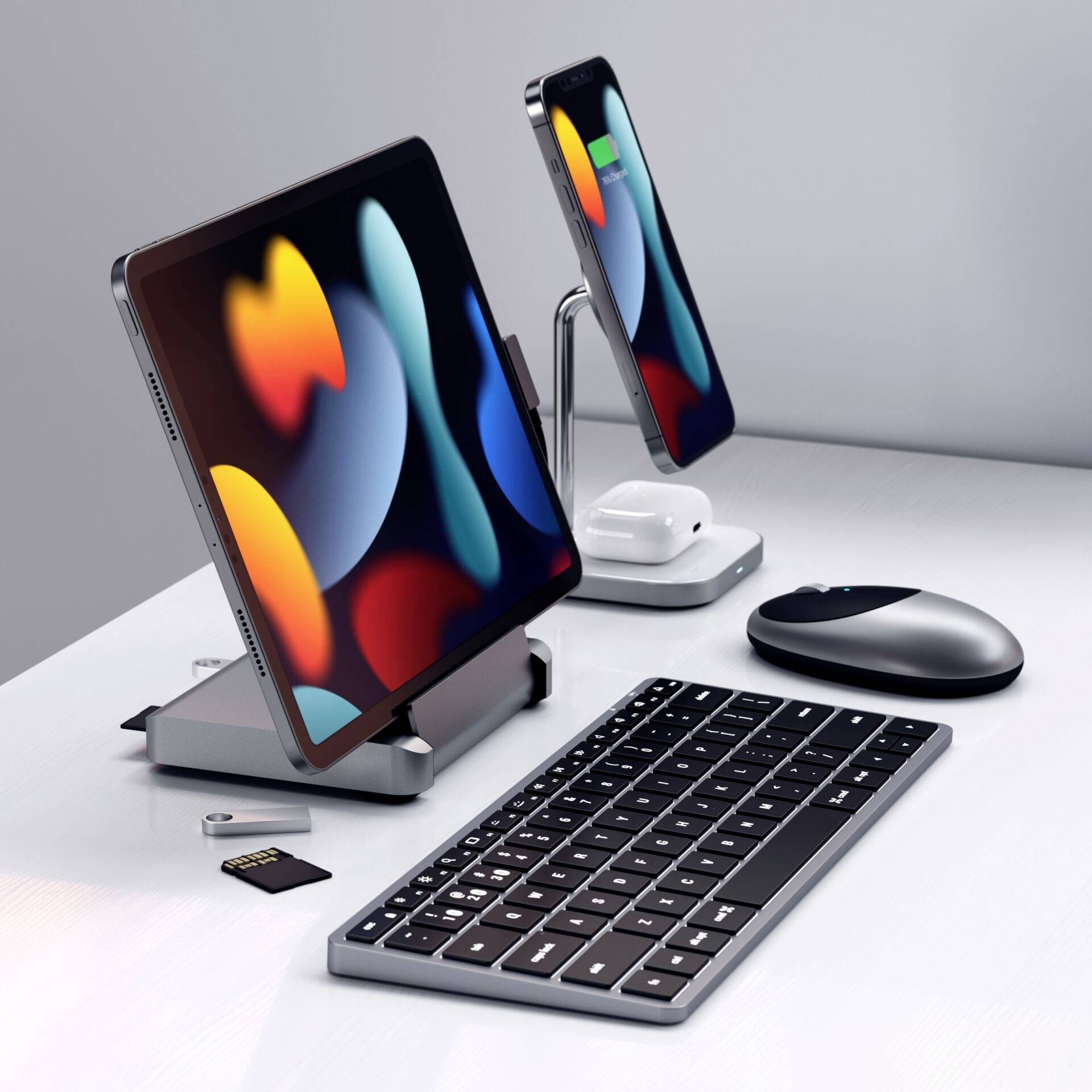 Tablet a smartphone na stojanech, vedle klávesnice, myš a paměťové karty. Moderní, minimalistické uspořádání pracovního stolu.