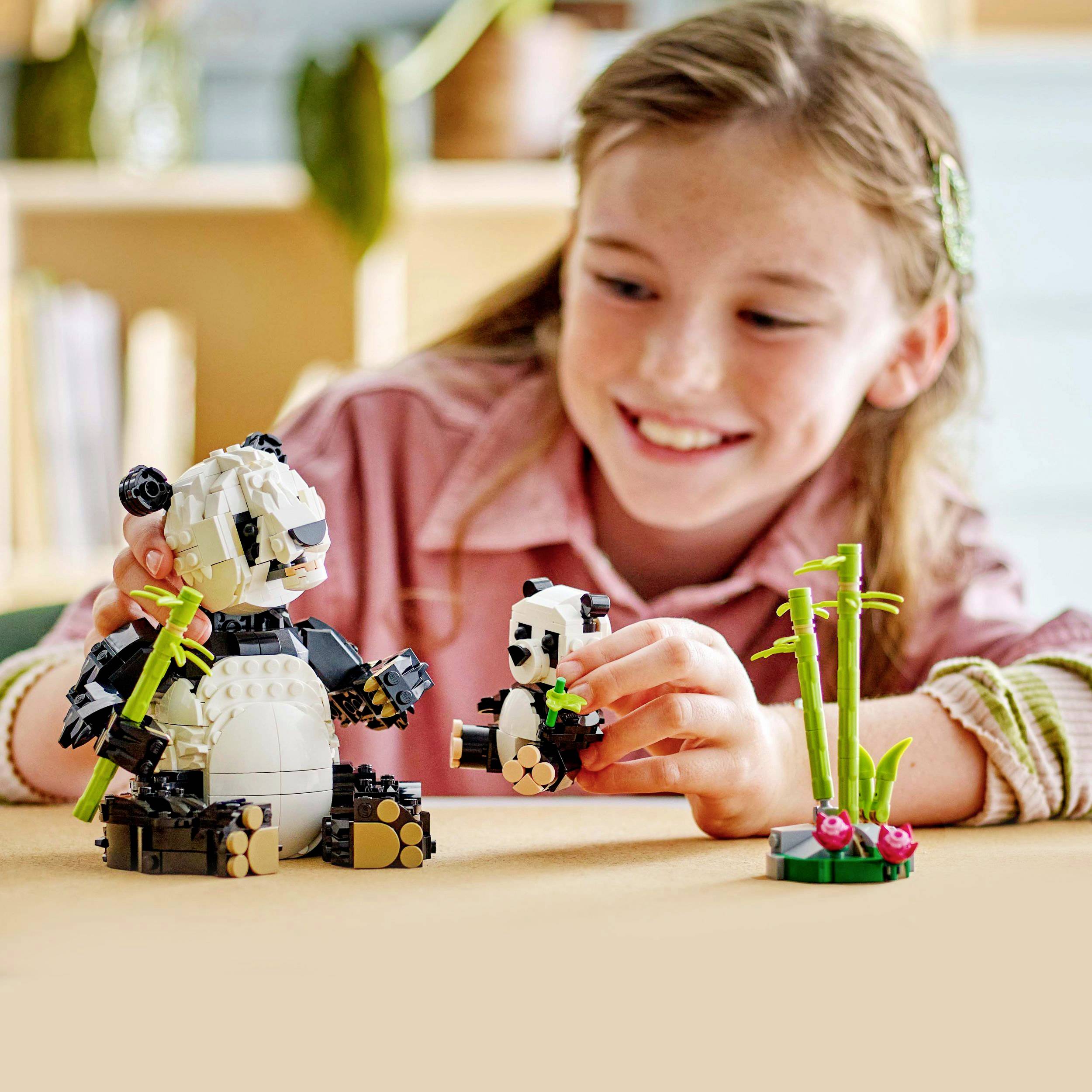 Dítě staví dva pandy z LEGO kostek, jednoho velkého a jednoho malého, na stole. V pozadí rozmazané prostředí.