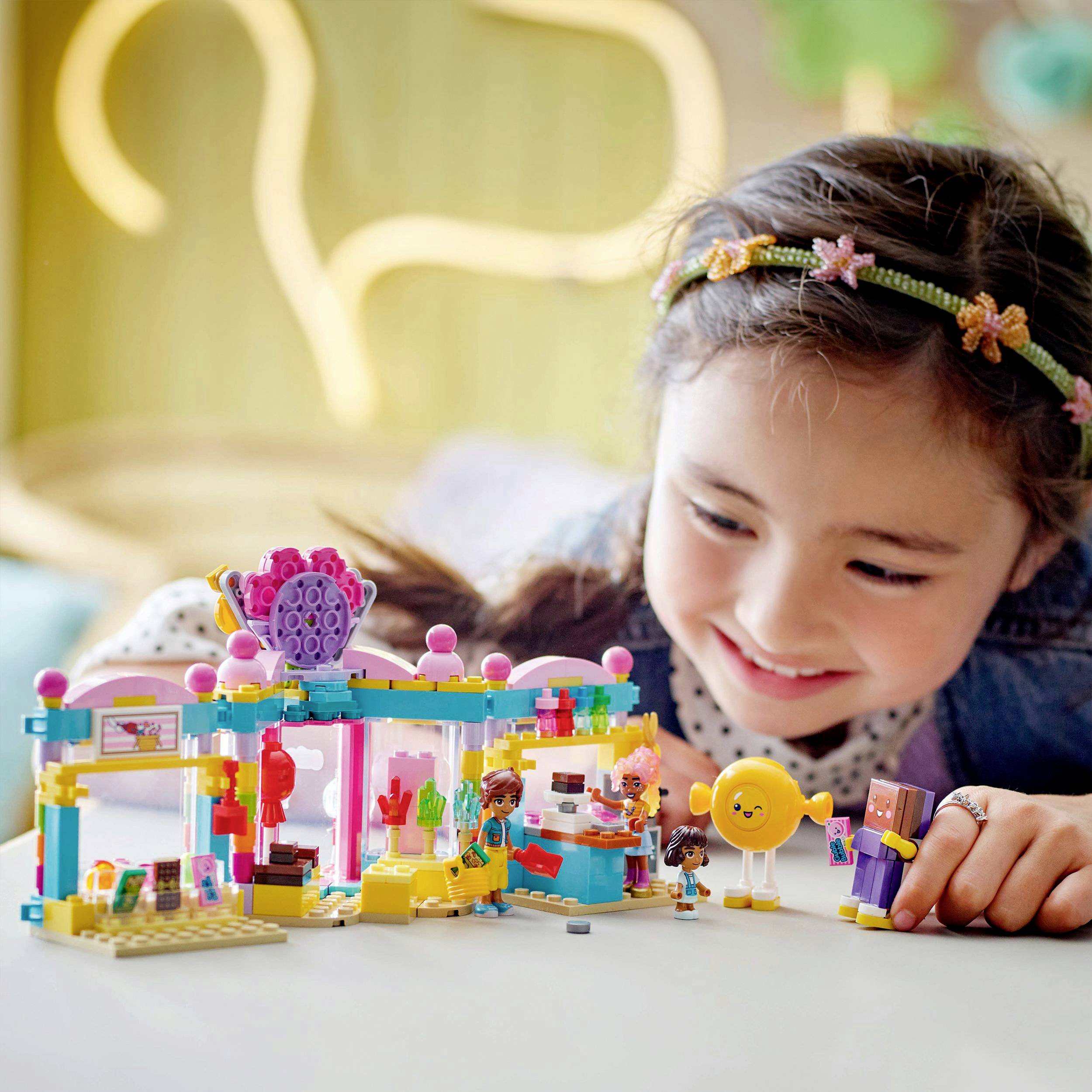 Dítě se usmívá, když si hraje s barevnou sadou Lego, která představuje malou kuchyň, s figurkami a dekoracemi.