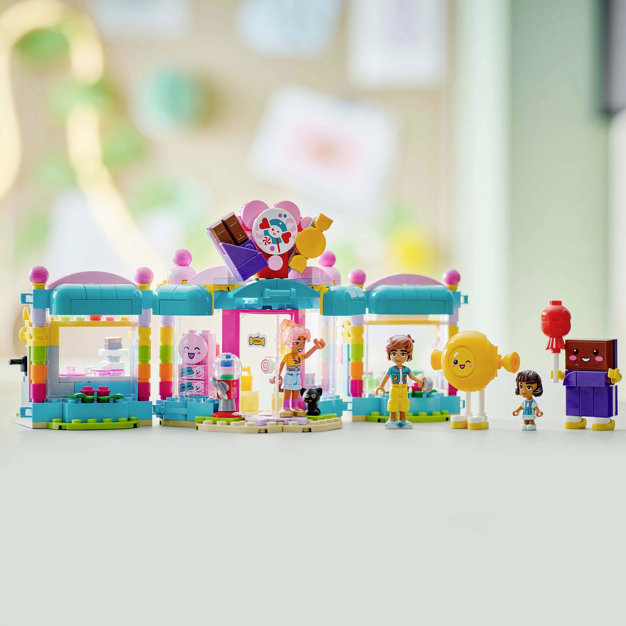 Barevná sada Lego stavebnice s figurkami, která zobrazuje veselou scénu v malé budově. Děti stojí kolem hračkářství.