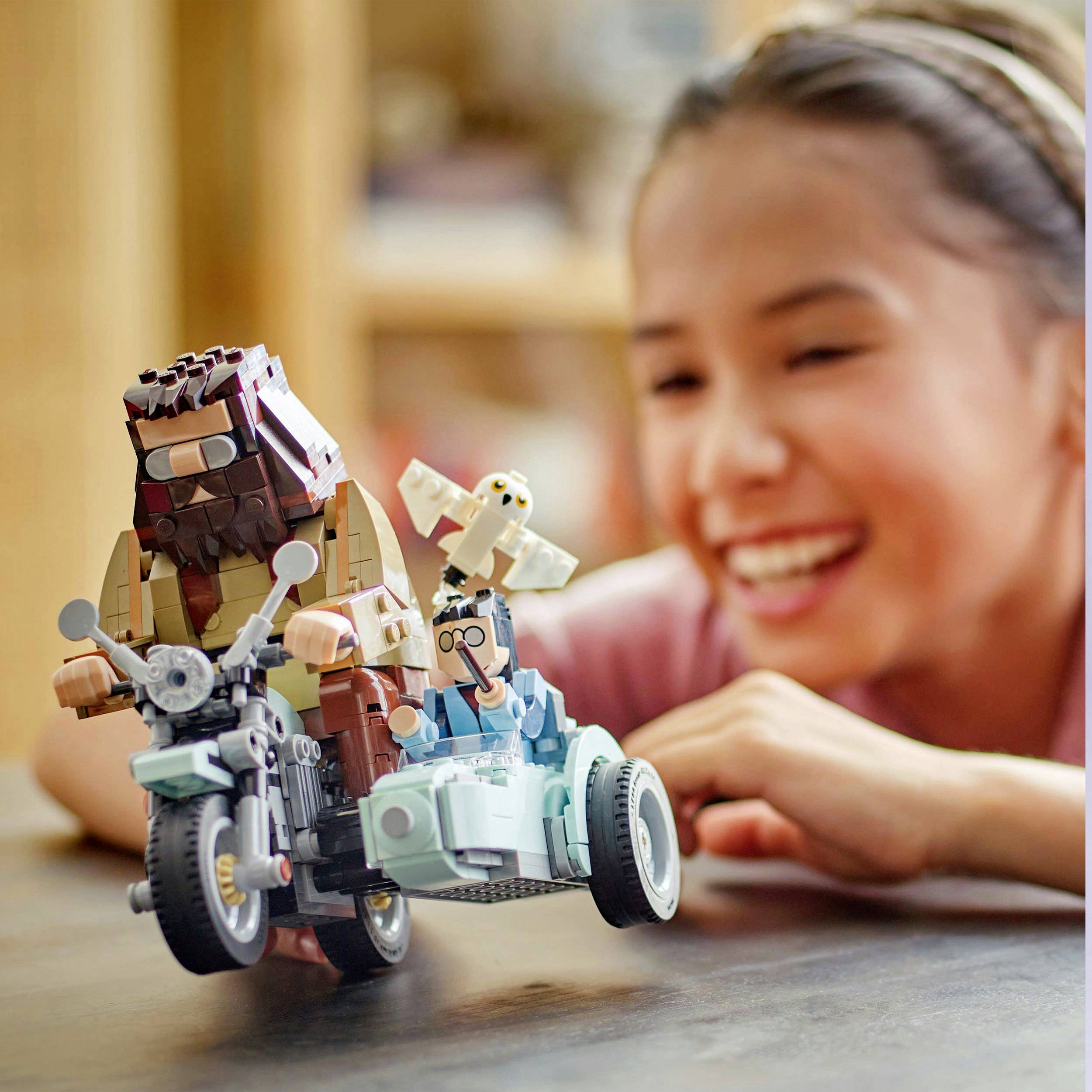 Dítě soustředěně si hraje s Lego sadou obsahující dvě motorky a figurky, včetně medvěda a racka. Pozadí je rozmazané.
