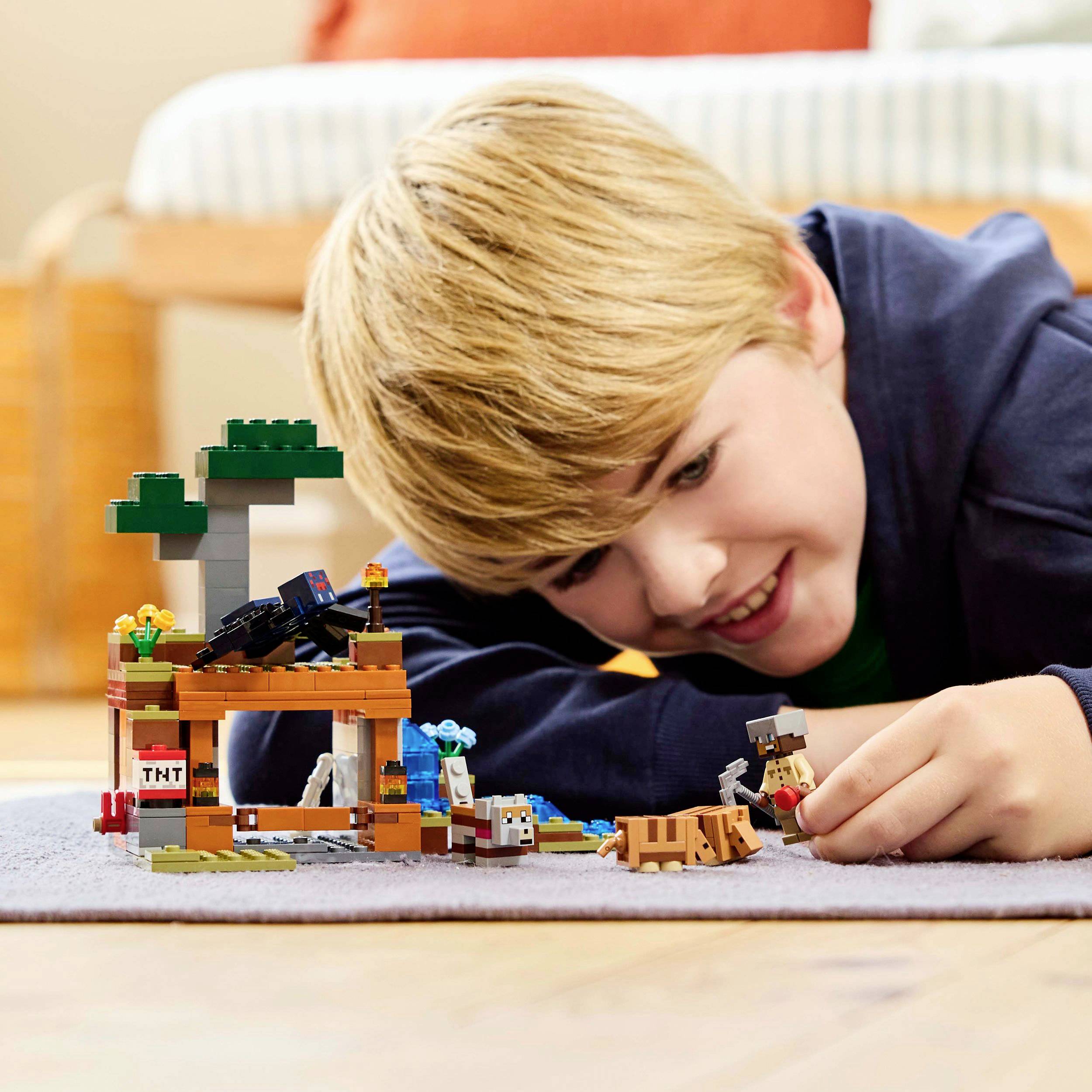 Dítě si hraje na koberci se sadou Minecraft, která obsahuje figurky, zvířata a TNT bednu v popředí.