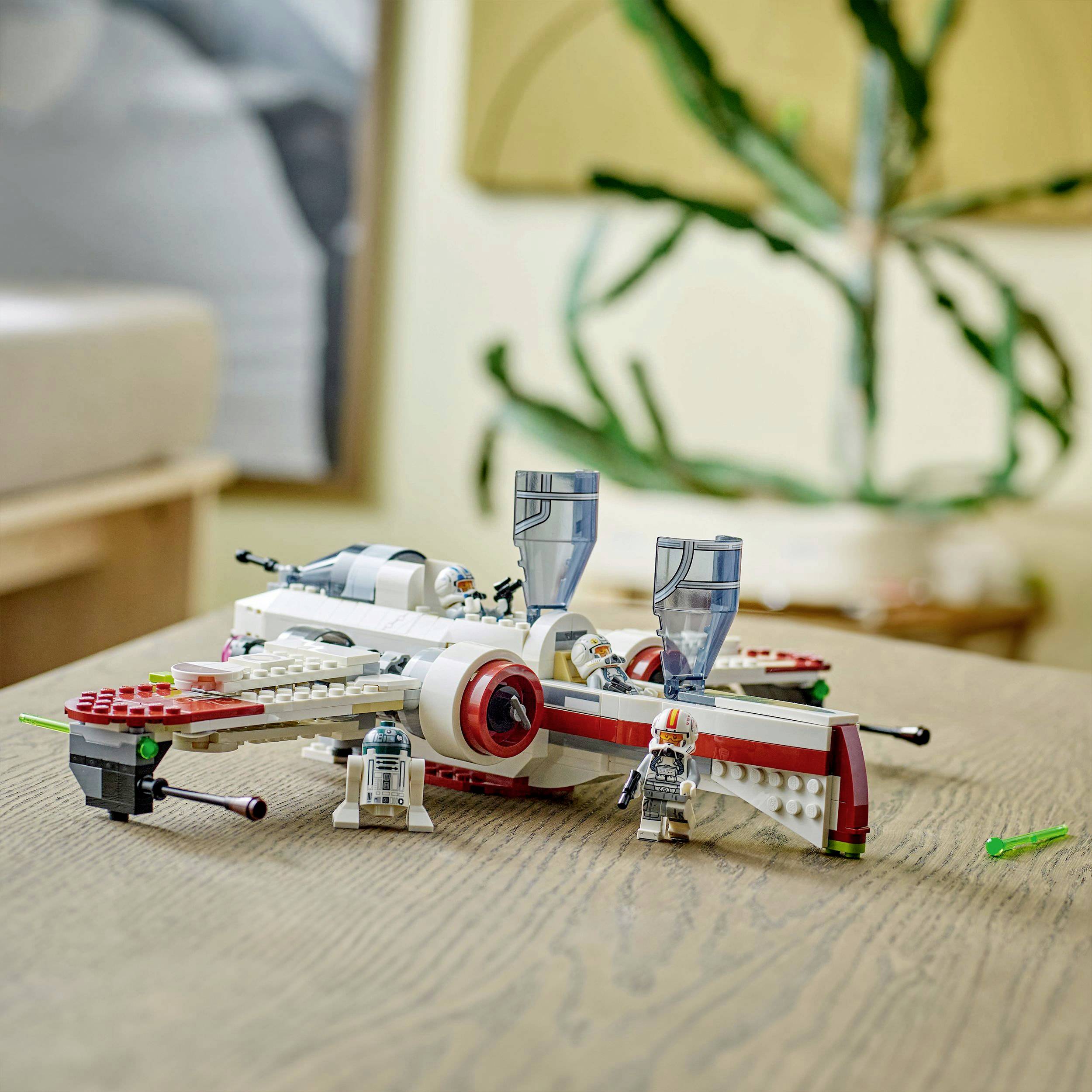 Vesmírná loď z LEGA se dvěma miniaturními figurkami, včetně robota a pilota, stojí na dřevěném stole. V pozadí je rozostřeno.