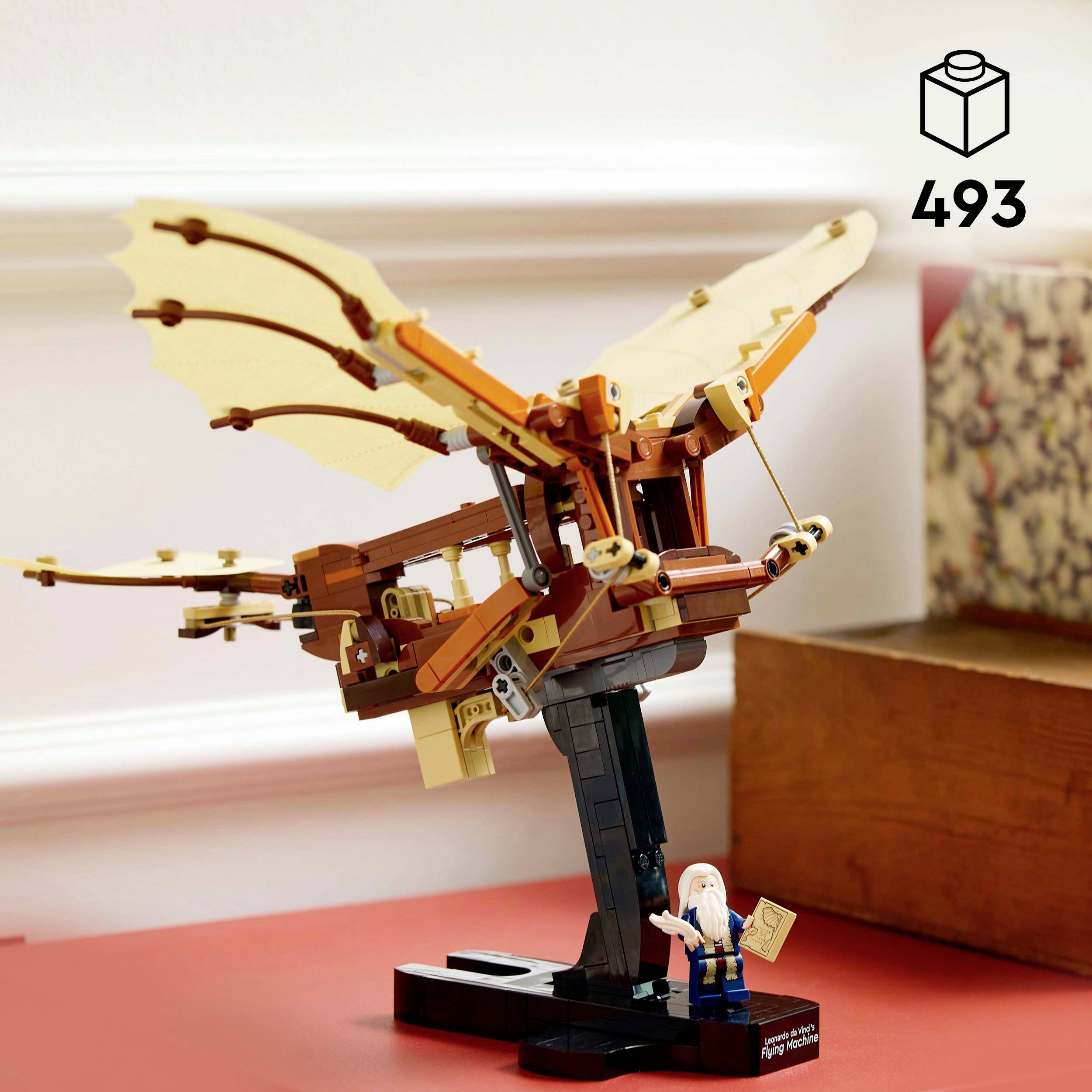 Lego stavebnice s hnědou létající bytostí na podstavci. Vedle stojí malá figurka s bílými vlasy a papírem v ruce.