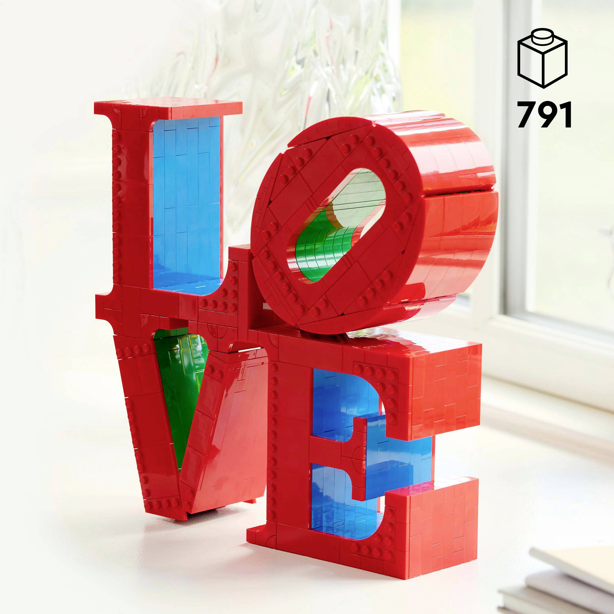 Červené Lego kostky tvoří slovo 'LOVE'. Světlé, moderní prostředí.