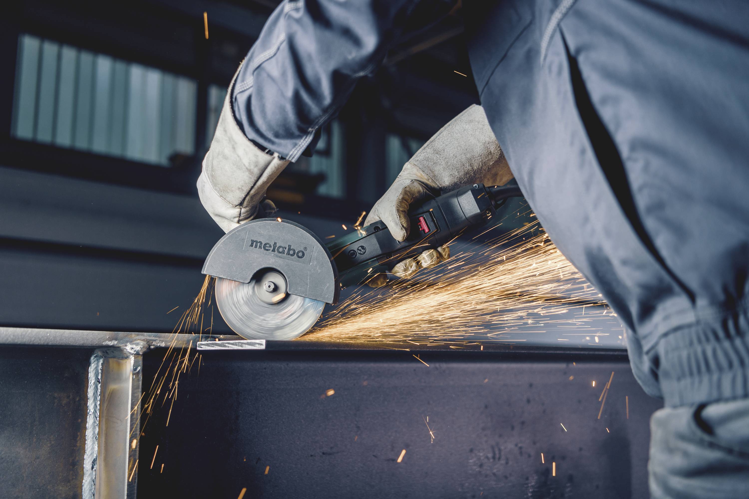 Osoba řeže kov elektrickým pilníkem, přičemž z místa řezání odletují jiskry. Je používáno bezpečnostní vybavení, aby bylo zajištěno maximální bezpečí.