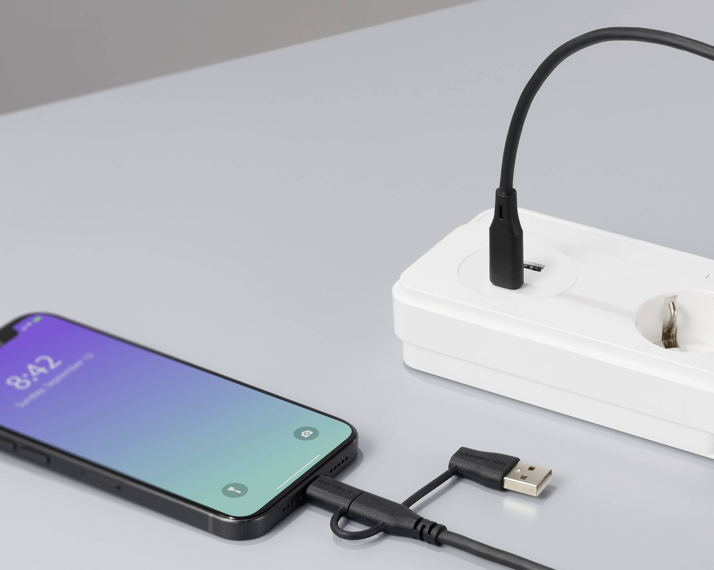 Mobilní telefon se nabíjí přes USB kabel zapojen do elektrické zásuvky. Na displeji je zobrazeno 8:42.