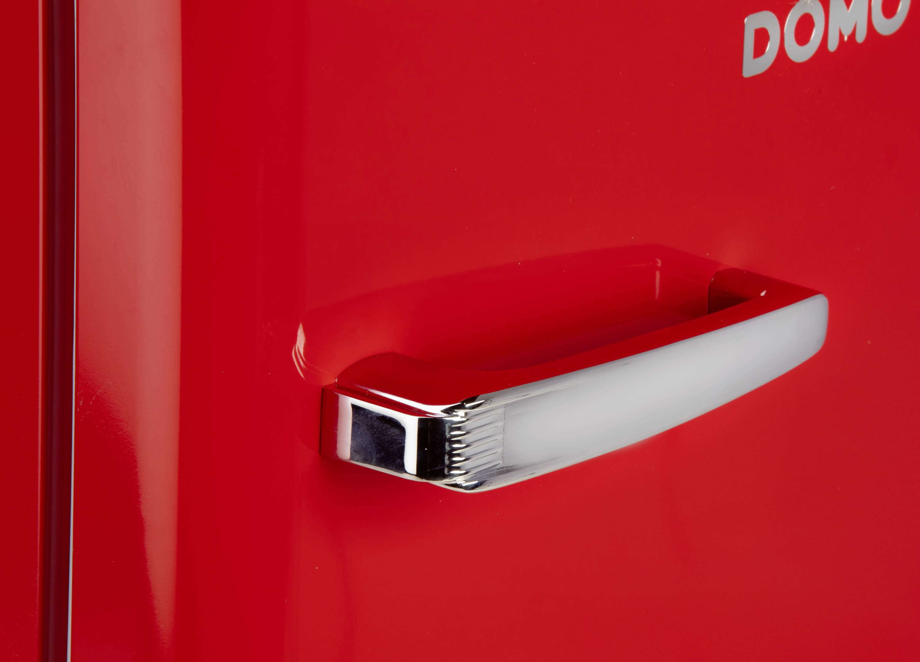 Červená lednice se stříbrnou rukojetí. Vpravo nahoře je nápis "DOMO". Design působí retro a minimalisticky.