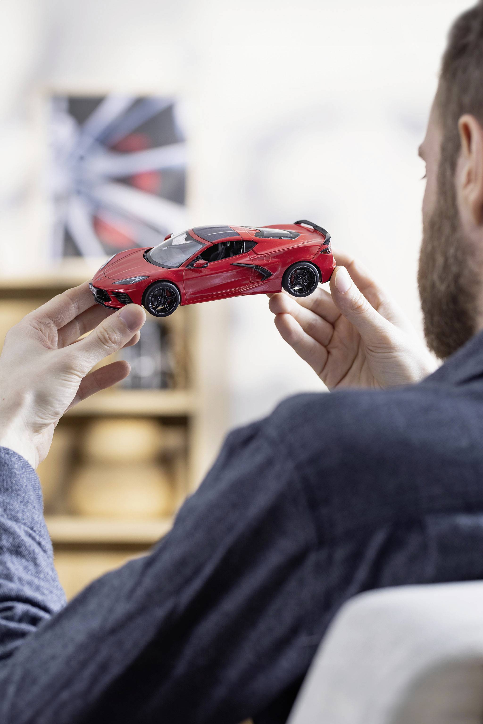 Osoba drží model auta v červené barvě. Auto je detailní a okolí je rozmazané, což klade důraz na samotné vozidlo.