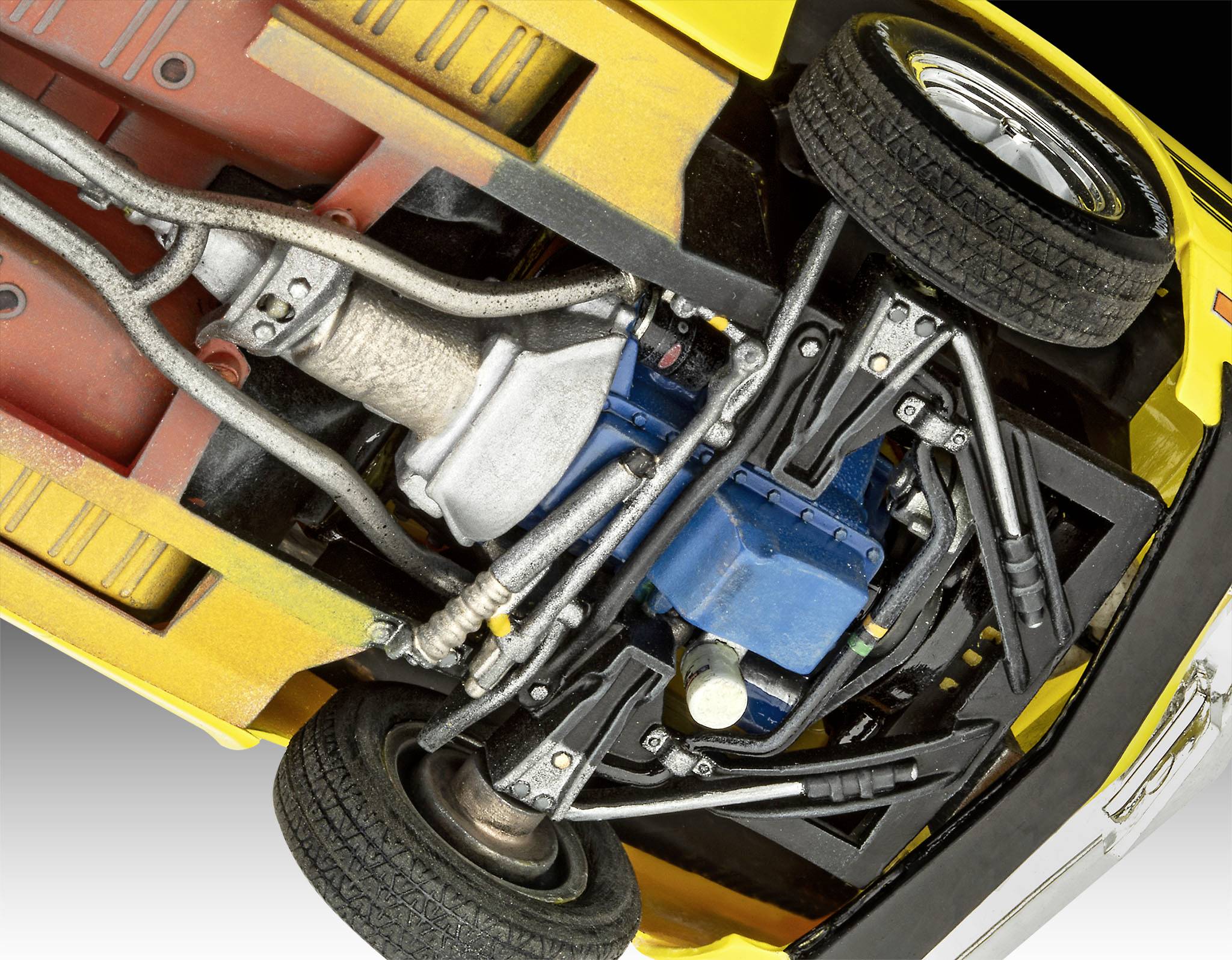 Obrázek ukazuje spodní stranu modelového autíčka, na kterém jsou viditelné podvozek, motor a části výfukového systému.