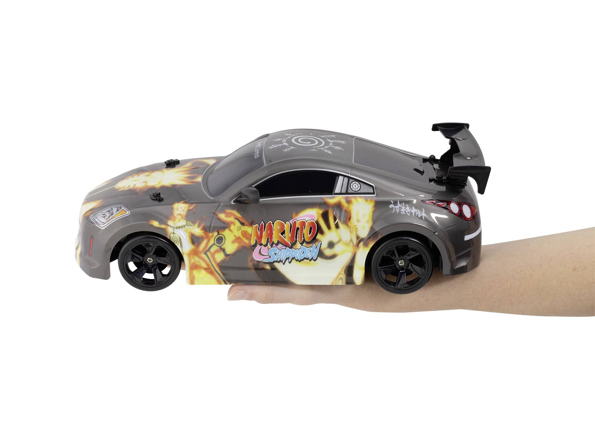 Dálkově ovládané auto ve stylu 'Naruto Shippuden' na napřažené ruce. Auto má šedý podvozek s výraznými grafickými prvky.