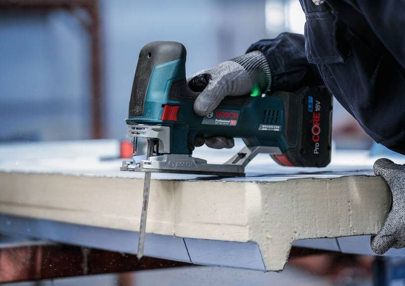 Osoba řeže pěnový materiál elektrickou přímočarou pilou. Důraz je kladen na řezací práci v prostředí dílny.