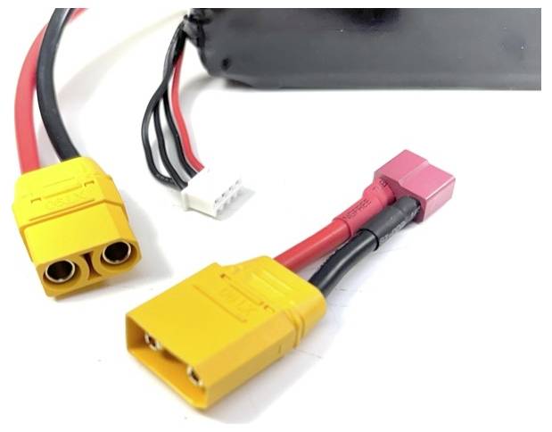 Žluté a červené elektrické konektory s vedením, propojené s černým zařízením v pozadí, na bílém podkladu.