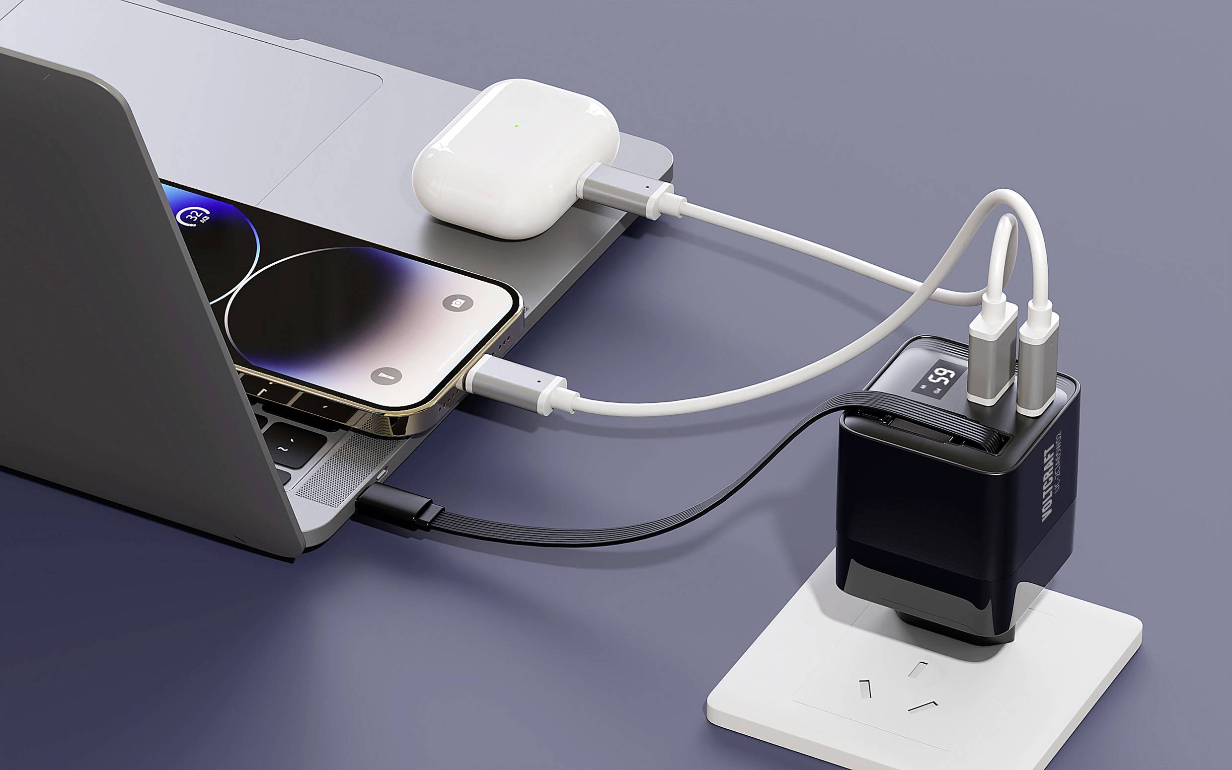 Laptop a smartphone jsou připojeny k nabíječce. Vedle leží otevřené pouzdro s bezdrátovými sluchátky.