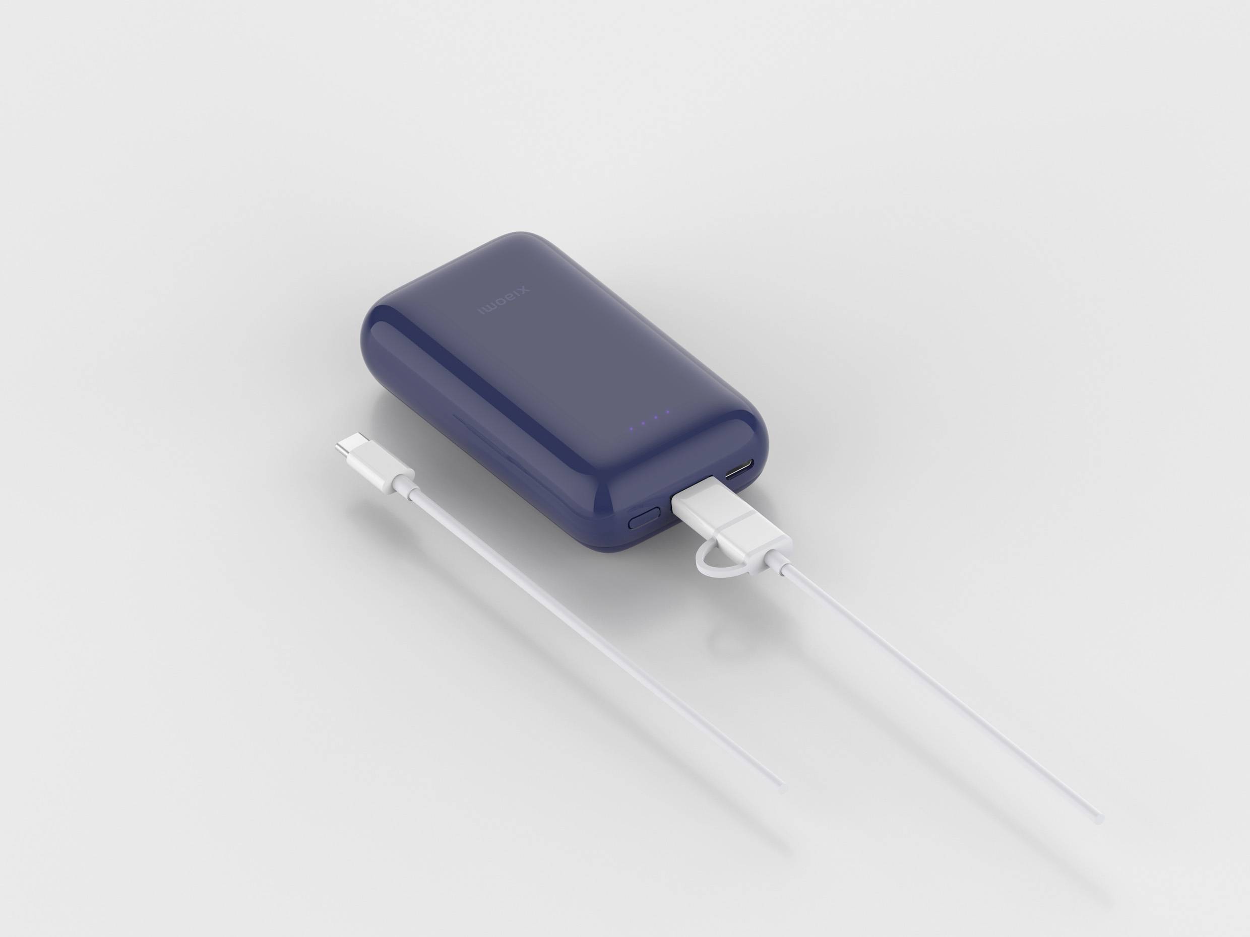 Tmavě modrá přenosná powerbanka s USB porty leží vedle bílého nabíjecího kabelu.