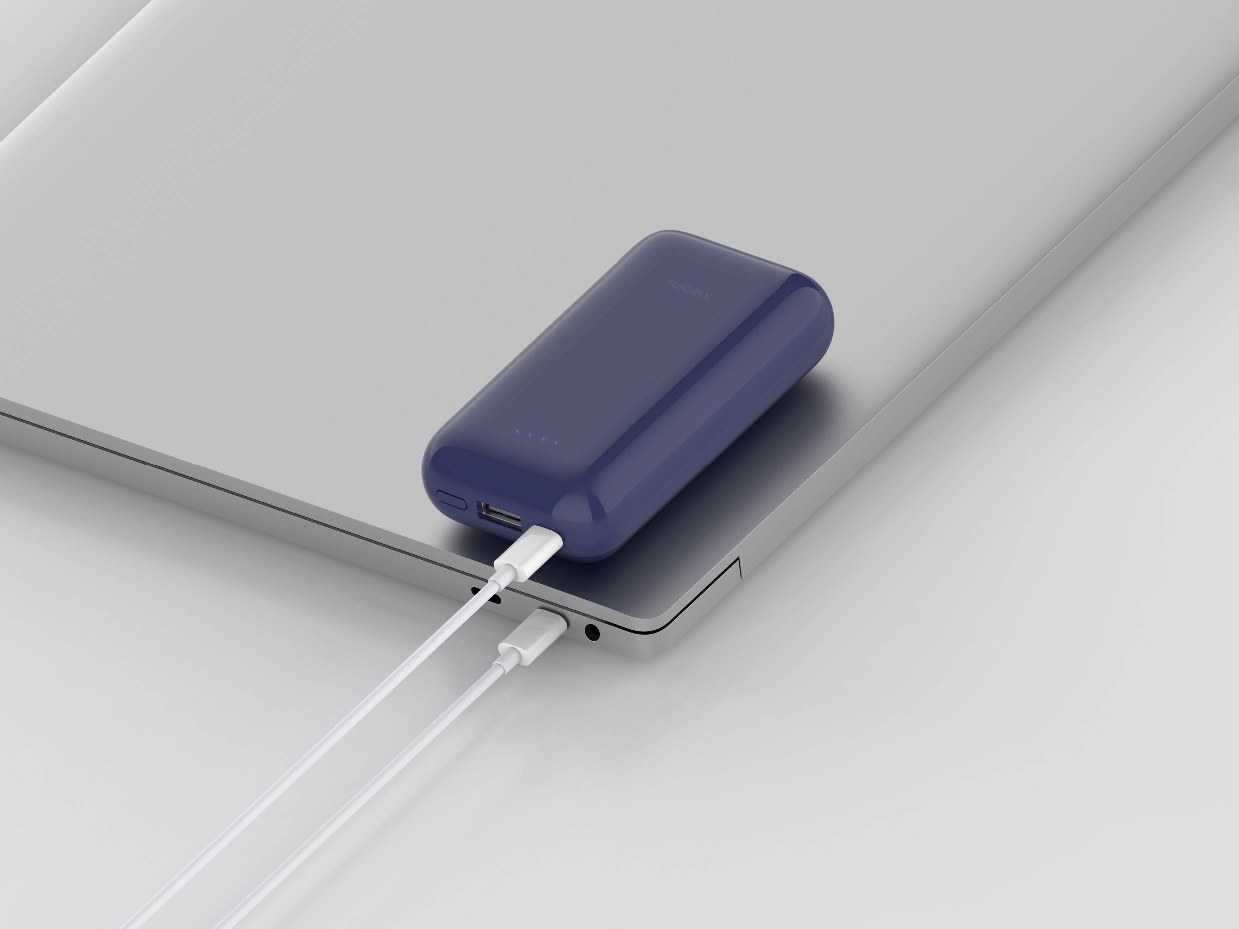 Powerbanka nabíjí laptop pomocí kabelu. Powerbanka leží na laptopu a zobrazuje své provozní indikátory.