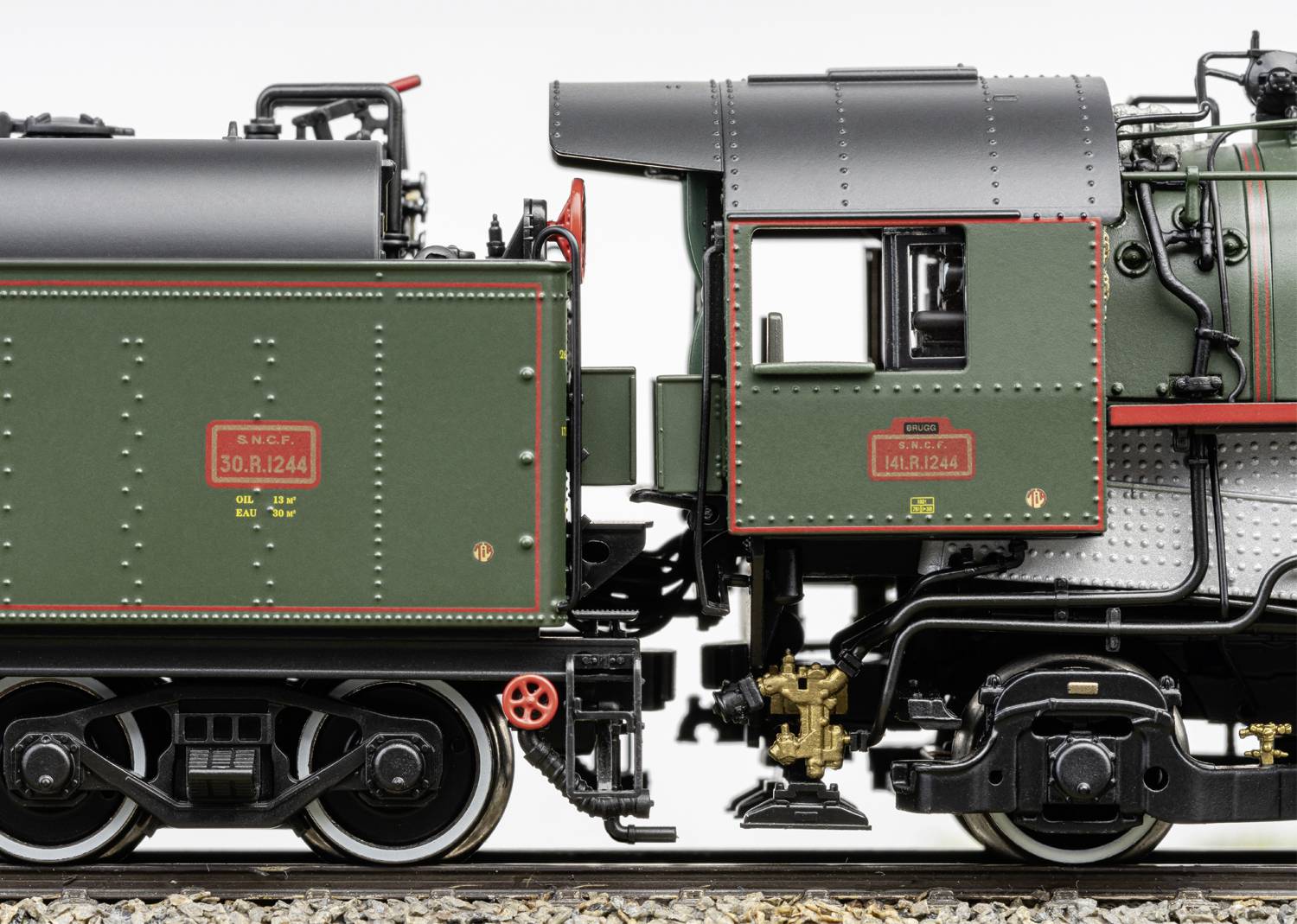 Detailní záběr modelové parní lokomotivy s tendrem, který je zobrazen v precizním zeleném laku s červenými a stříbrnými akcenty.