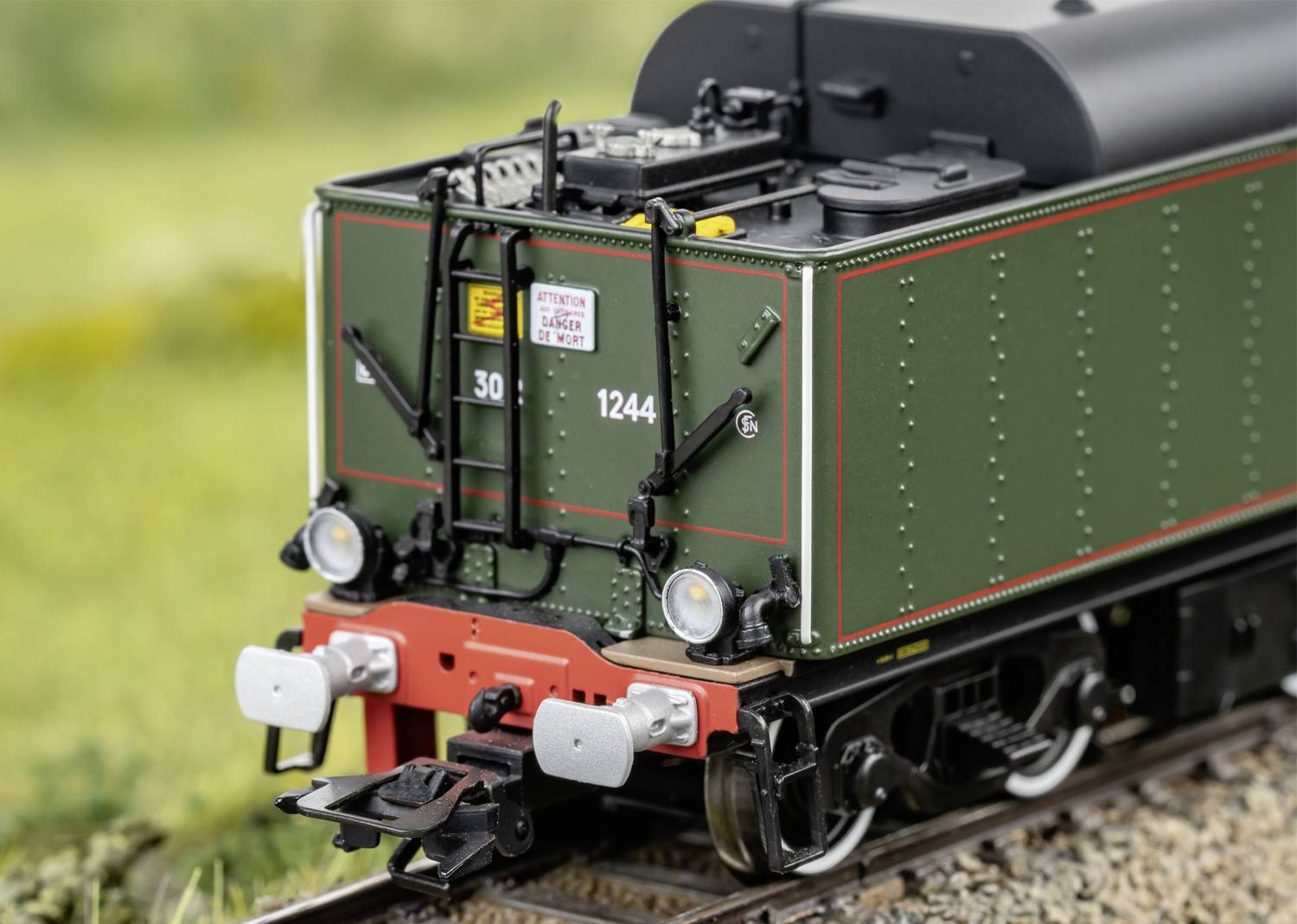 Model vlaku v zelené barvě s číslem '1244' stojí na kolejích v rurální krajině. Detailně a realisticky zpracovaný.