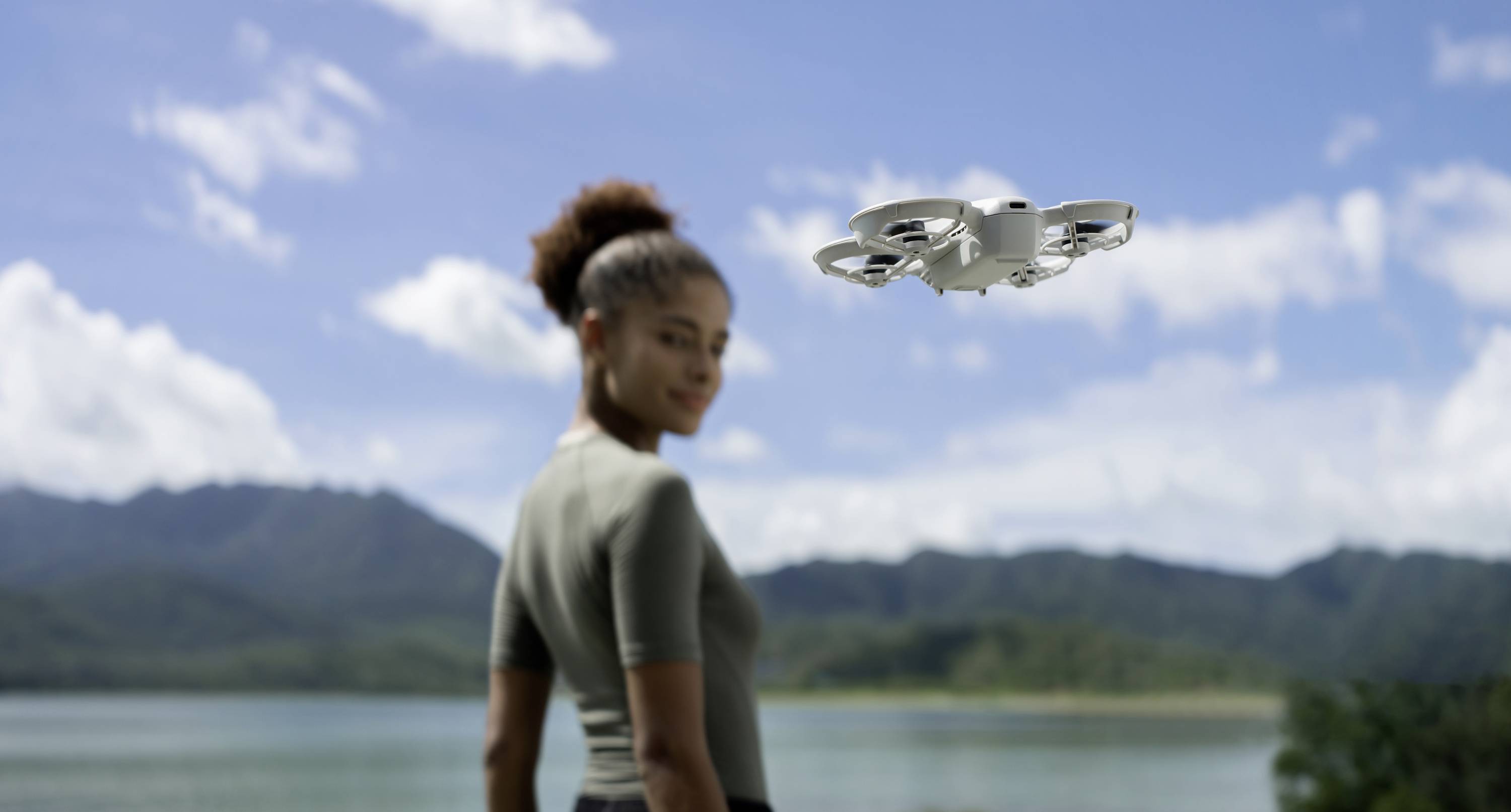 Žena se dívá na vznášející se dron před malebnou horskou a jezerní krajinou.