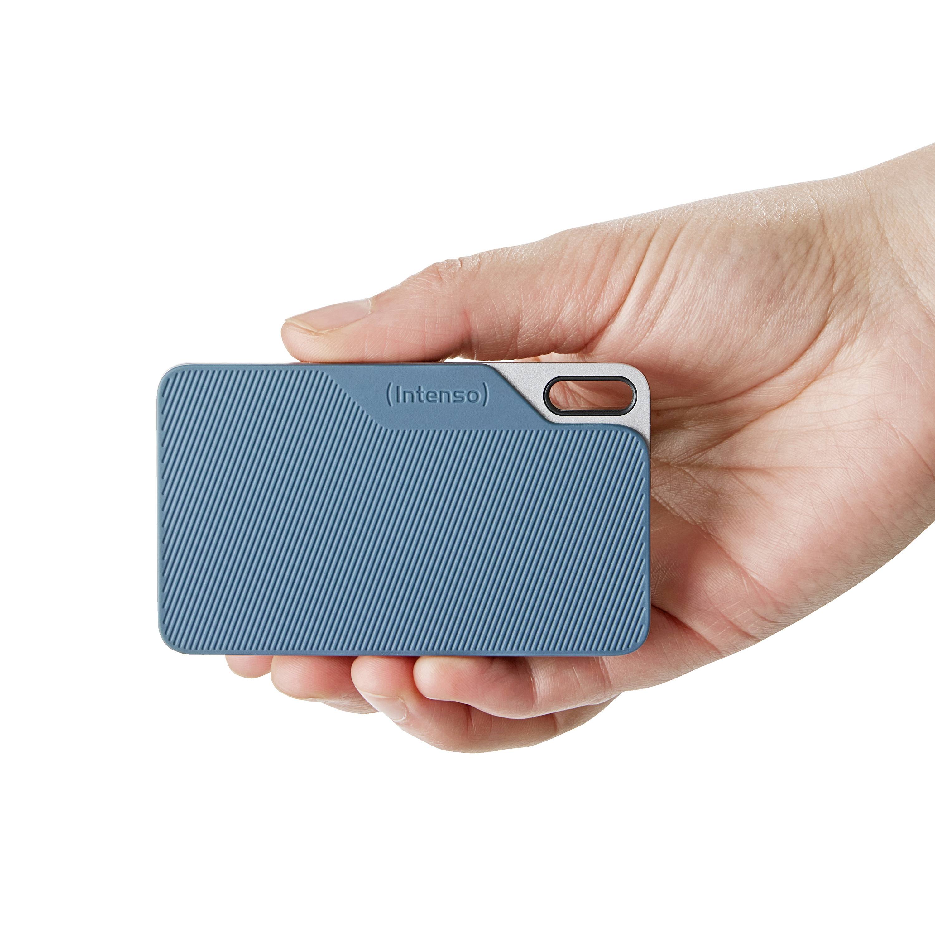 Jedna ruka drží modrou přenosnou externí disk Intenso s vroubkovaným povrchem, což zdůrazňuje jeho přenositelnost a moderní design.