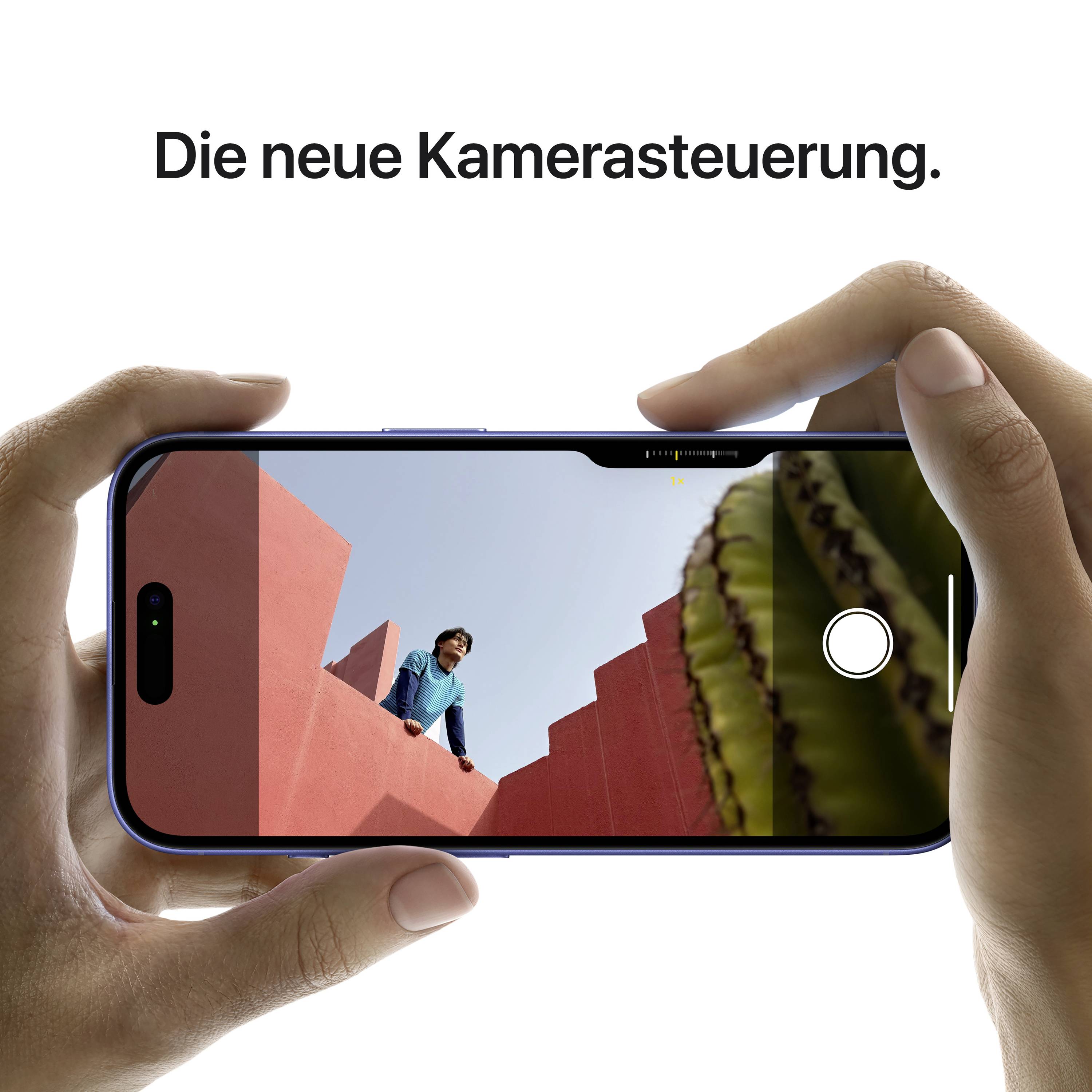 Smartphone je drženo dvěma rukama, zobrazuje kamerovou funkci se zaměřením na osobu v modré bundě před červenou budovou. Text nahoře: 'Nové ovládání kamery.'