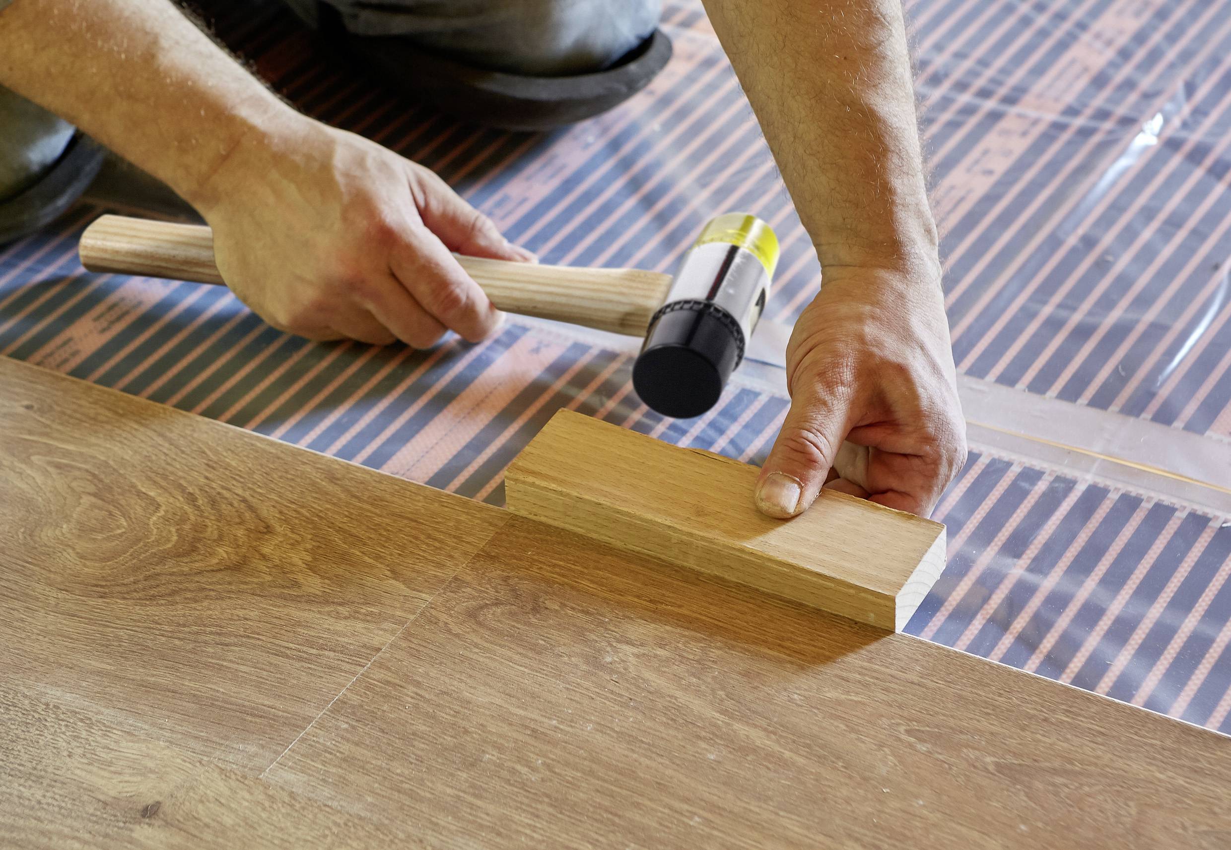 Řemeslník instaluje laminátovou podlahu, přičemž pečlivě upravuje dřevěnou desku gumovou palicí, aby zabránil mezerám.
