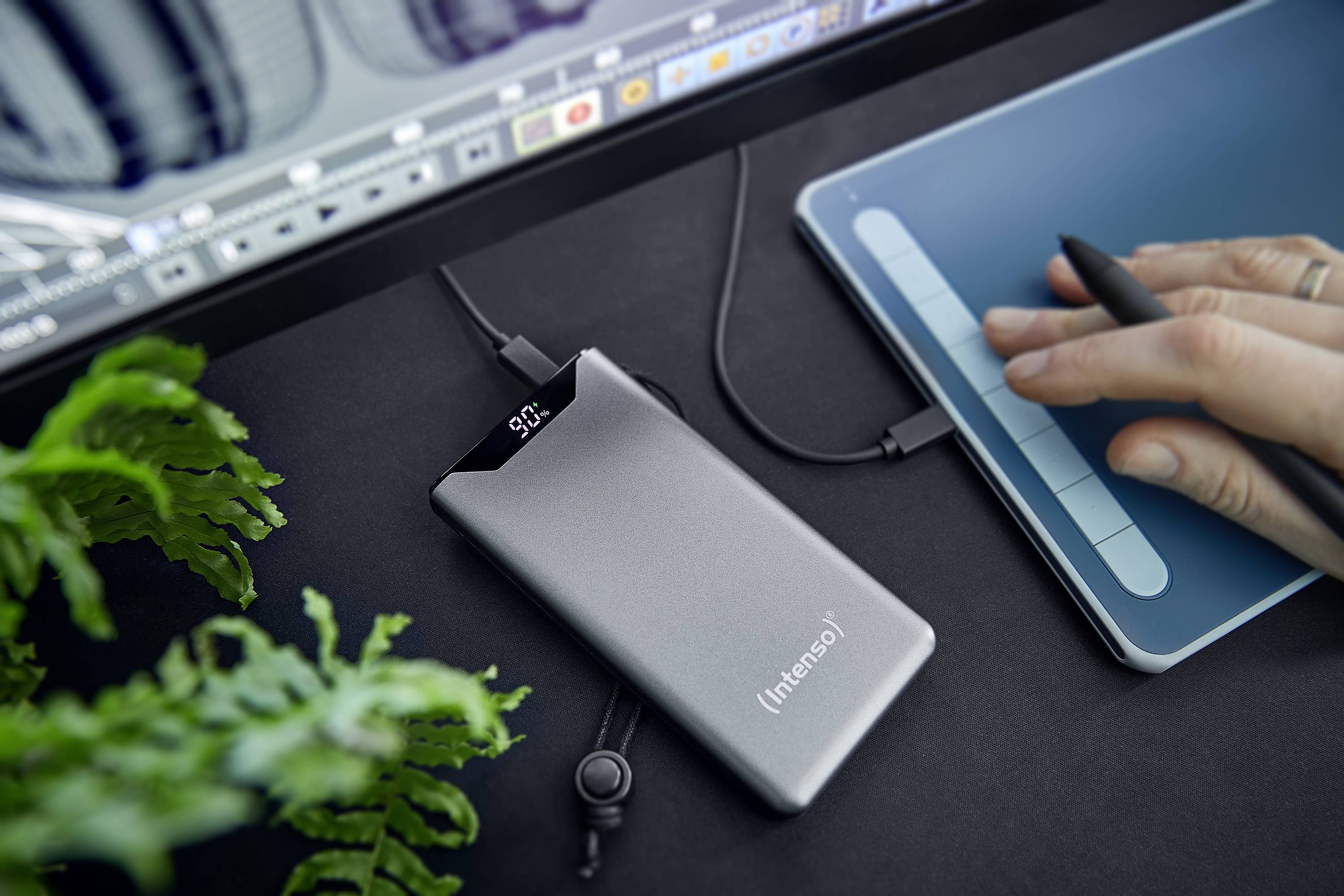 Externí stříbrný externí disk značky Intenso, připojený k počítači, umístěný na černém psacím stole vedle ruky používající grafický tablet.