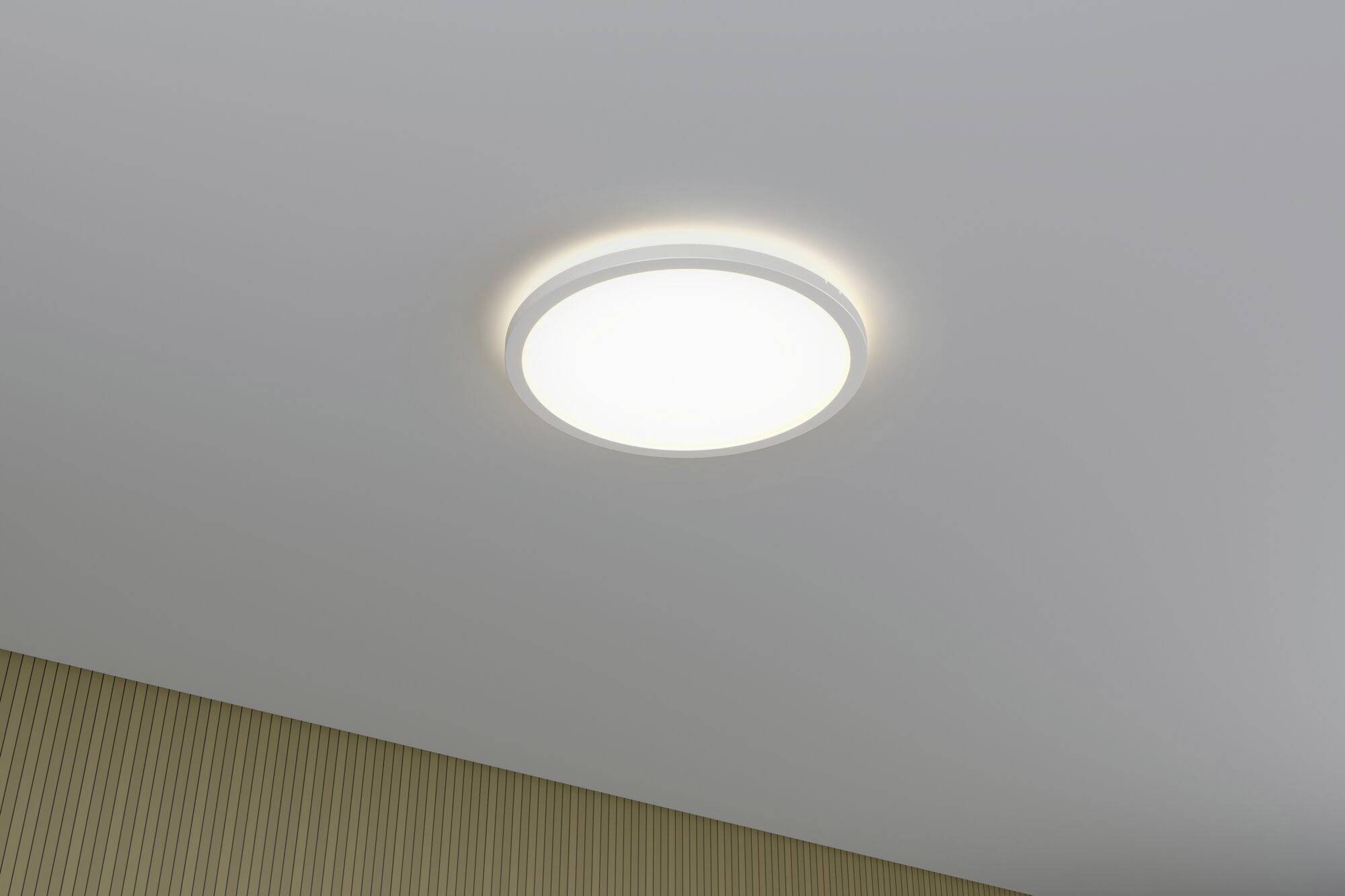 Kulatá stropní lampa s jemným světelným výstupem, umístěná na stropě nad stěnou s béžovými vertikálními pruhy.