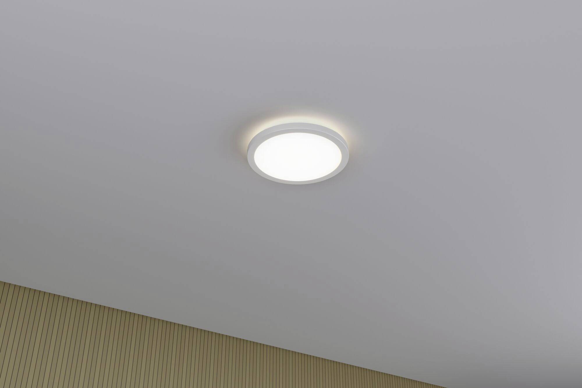 Kulatá stropní lampa svítí v místnosti s béžovými vertikálními pruhy na stěně.