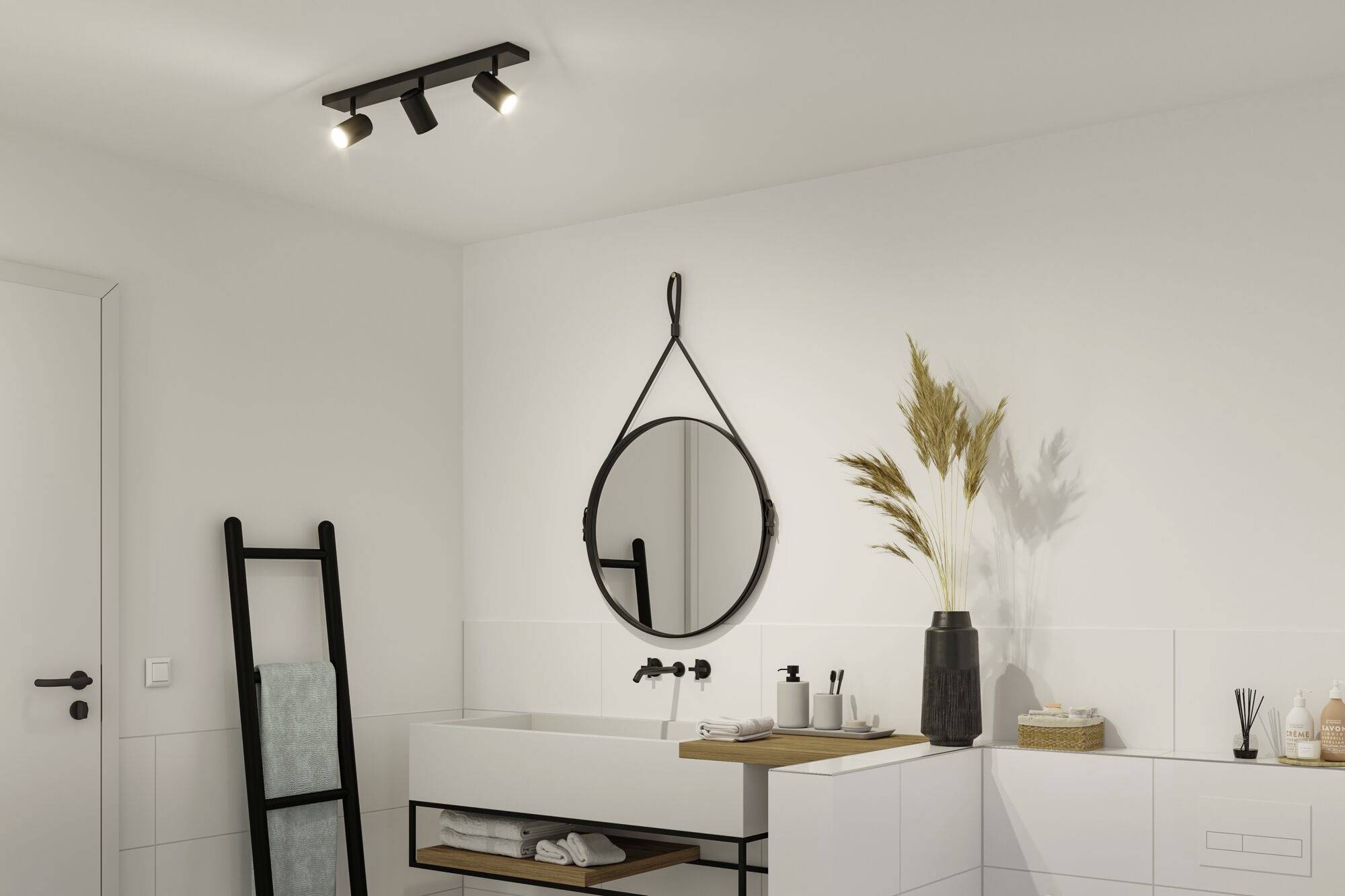 Moderní koupelna s kulatým zrcadlem na stěně, umyvadlem s černou baterií a dekorací sušených květin ve váze.
