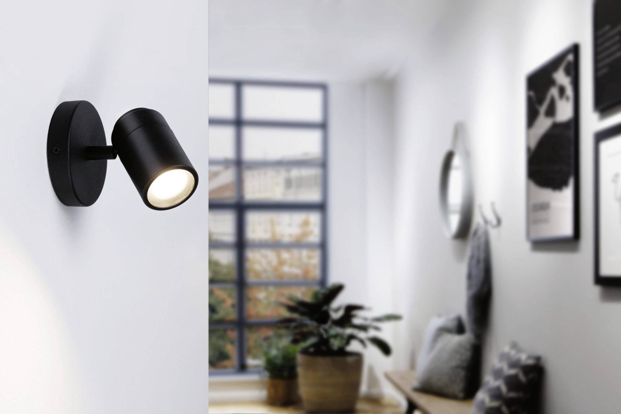 Černé nástěnné osvětlení v moderním prostoru s rostlinami a obrazy, osvětlující levou stěnu.