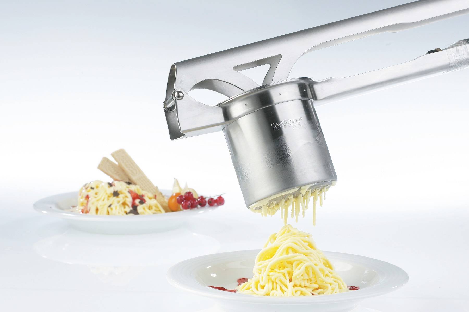 Stroj na spaghetti zmrzlinu vytlačuje vanilkovou zmrzlinu do tvaru špaget na talíř, v pozadí je hotový spaghetti zmrzlinový dezert.