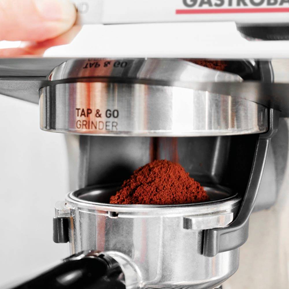 Detailní záběr na espresso stroj, který dávkuje čerstvě namletou kávovou mouku do páky. Nahoře je viditelný firemní nápis.