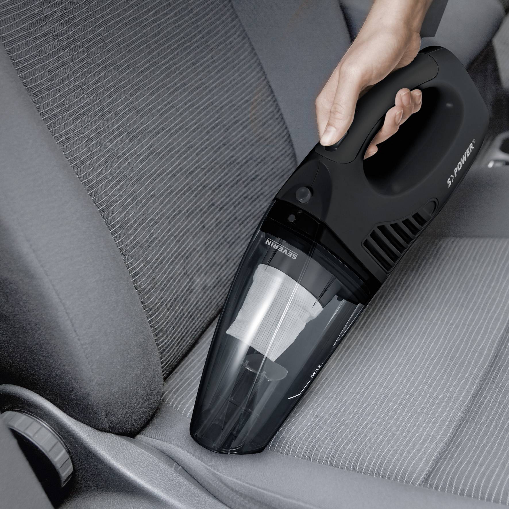 Ruka používá přenosný vysavač k čištění sedadla automobilu. Vysavač je černý a obratný.