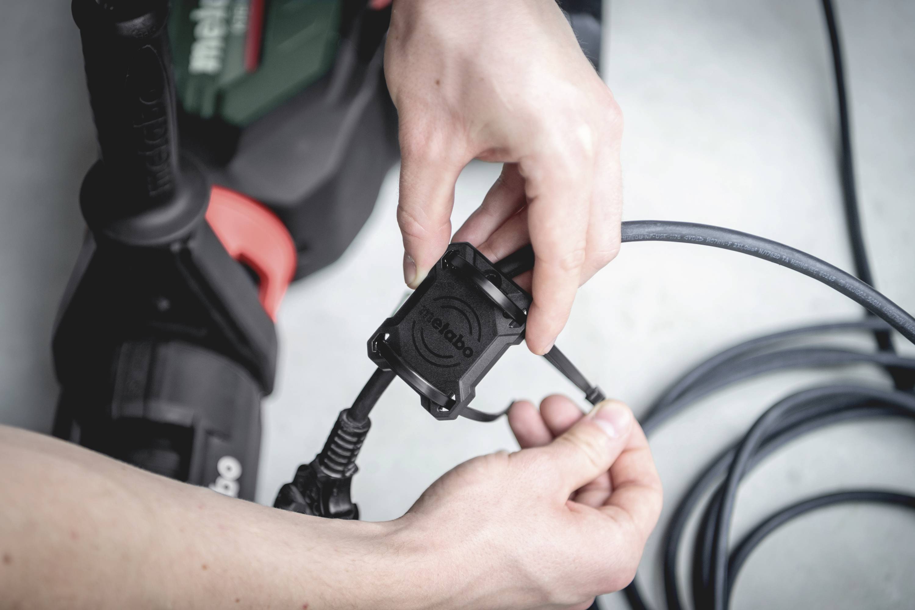 Osoba drží elektrické nářadí a připojuje kabel. Ruce upravují připojení. Ostrý fokus je na propojení a nástroje.